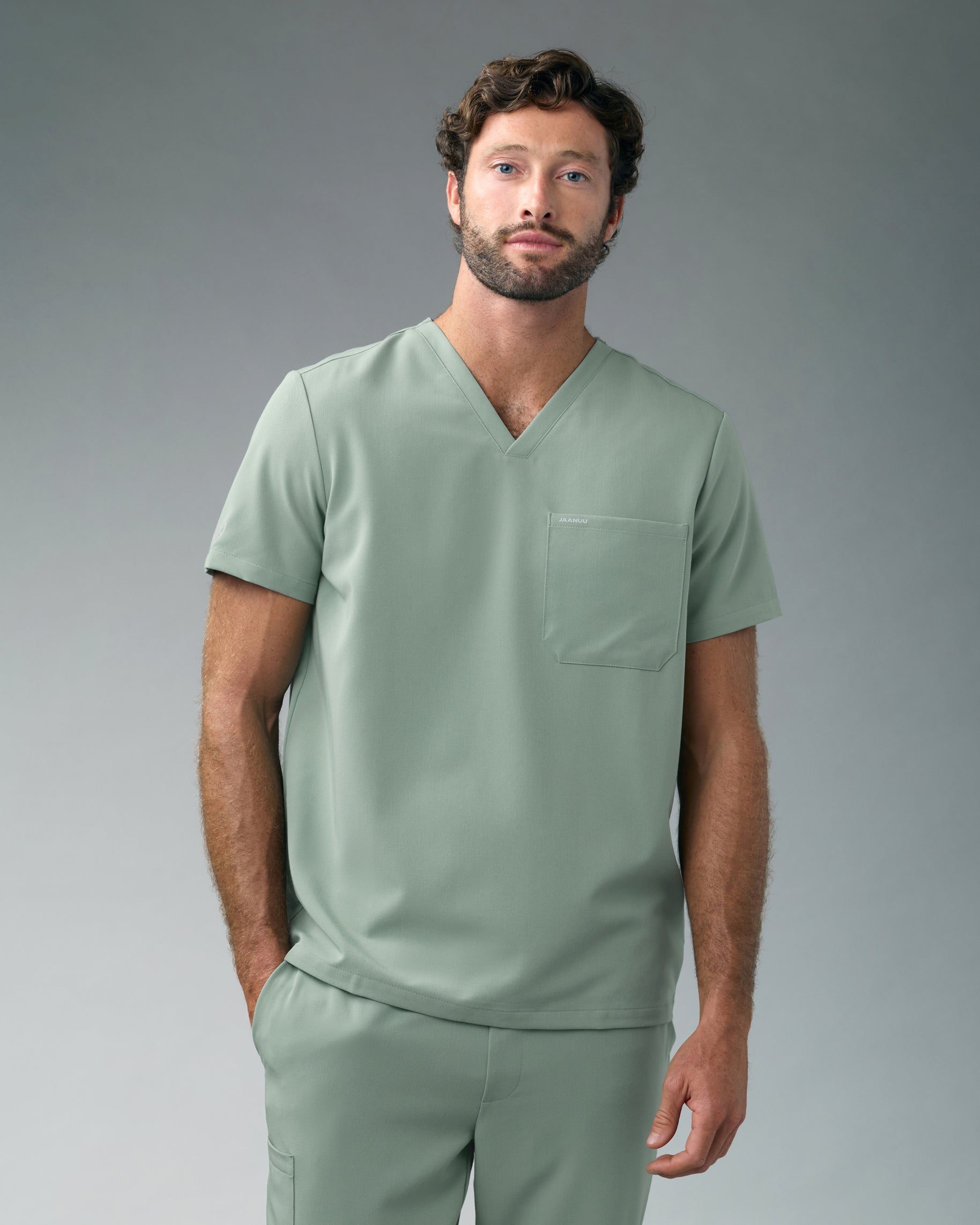 Man in a sage green V-neck scrub top with a chest pocket and matching scrub pants