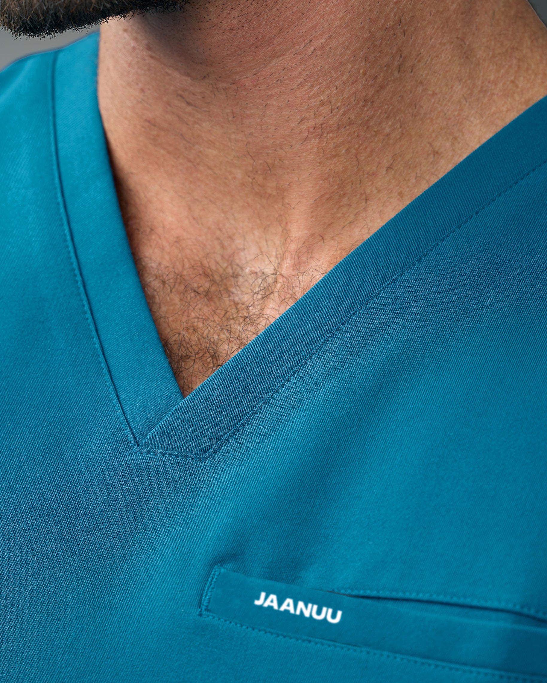 Close-up of the V-neckline of a teal scrub top with JAANUU on the chest welt pocket