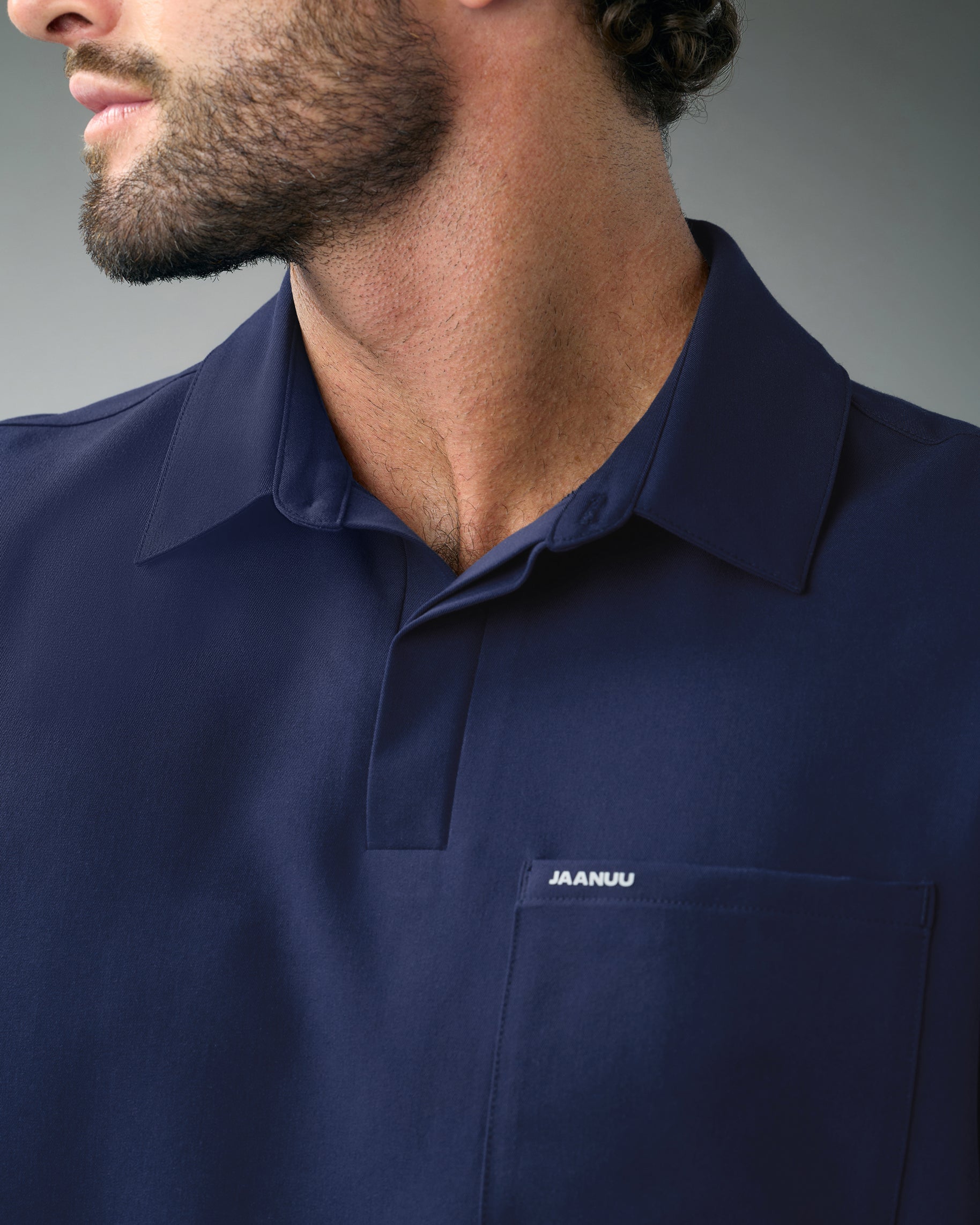 Close-up of the polo collar, placket and chest pocket marked JAANUU on a navy scrub top