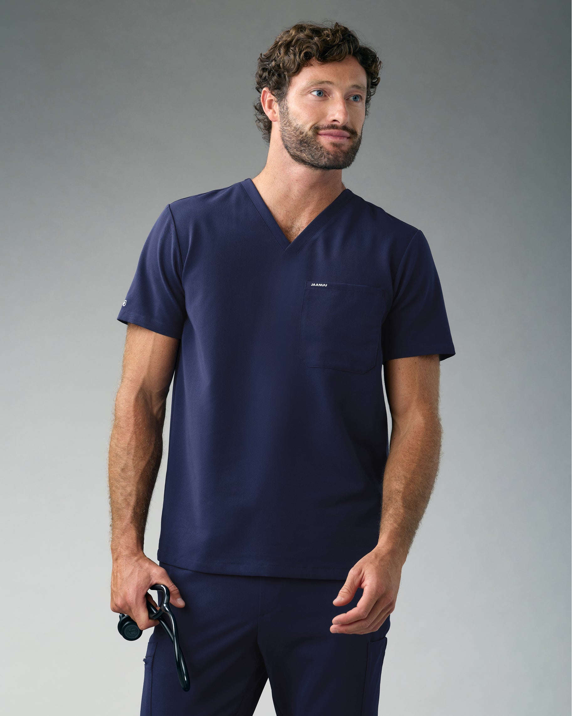 Man in a navy slim V-neck scrub top with a chest pocket and matching scrub pants, holding a stethoscope