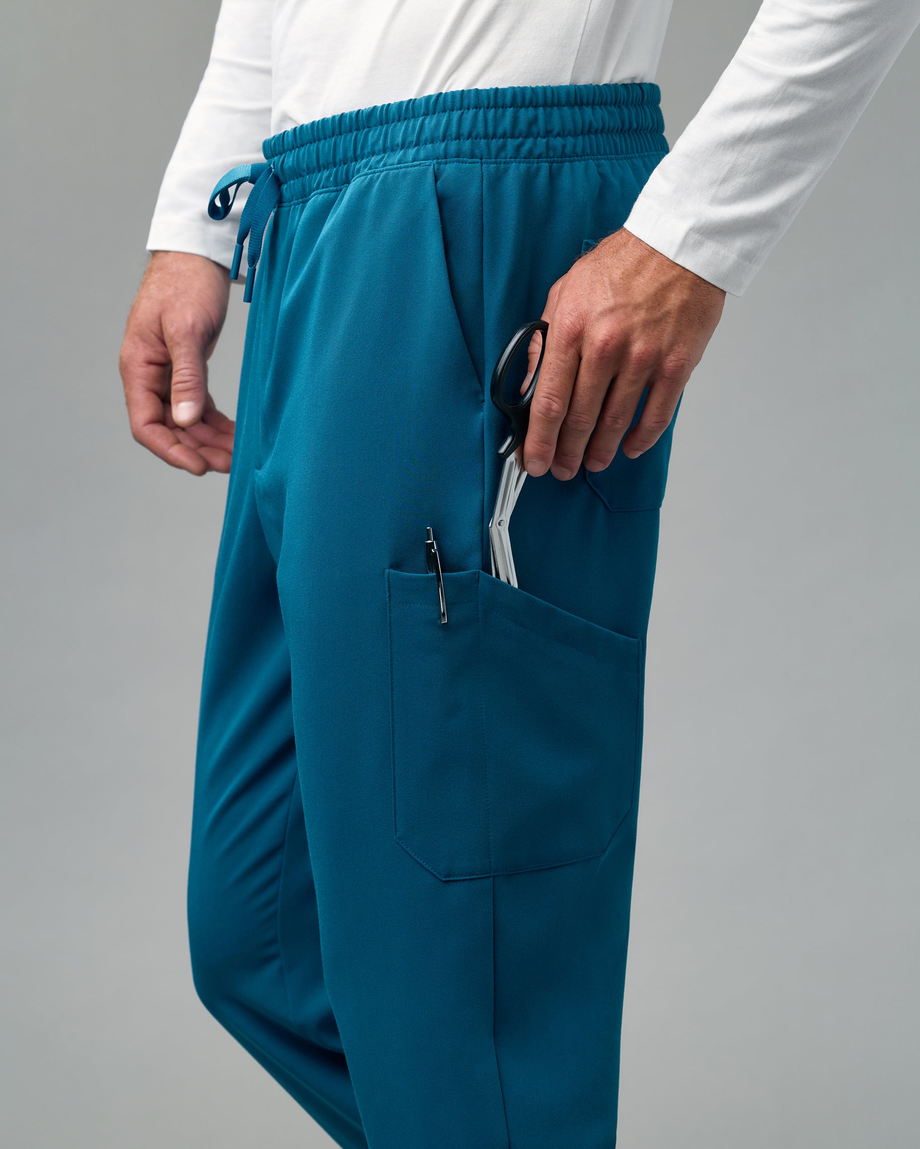 Close-up of trauma shears and a pen in the cargo pocket of teal scrub joggers