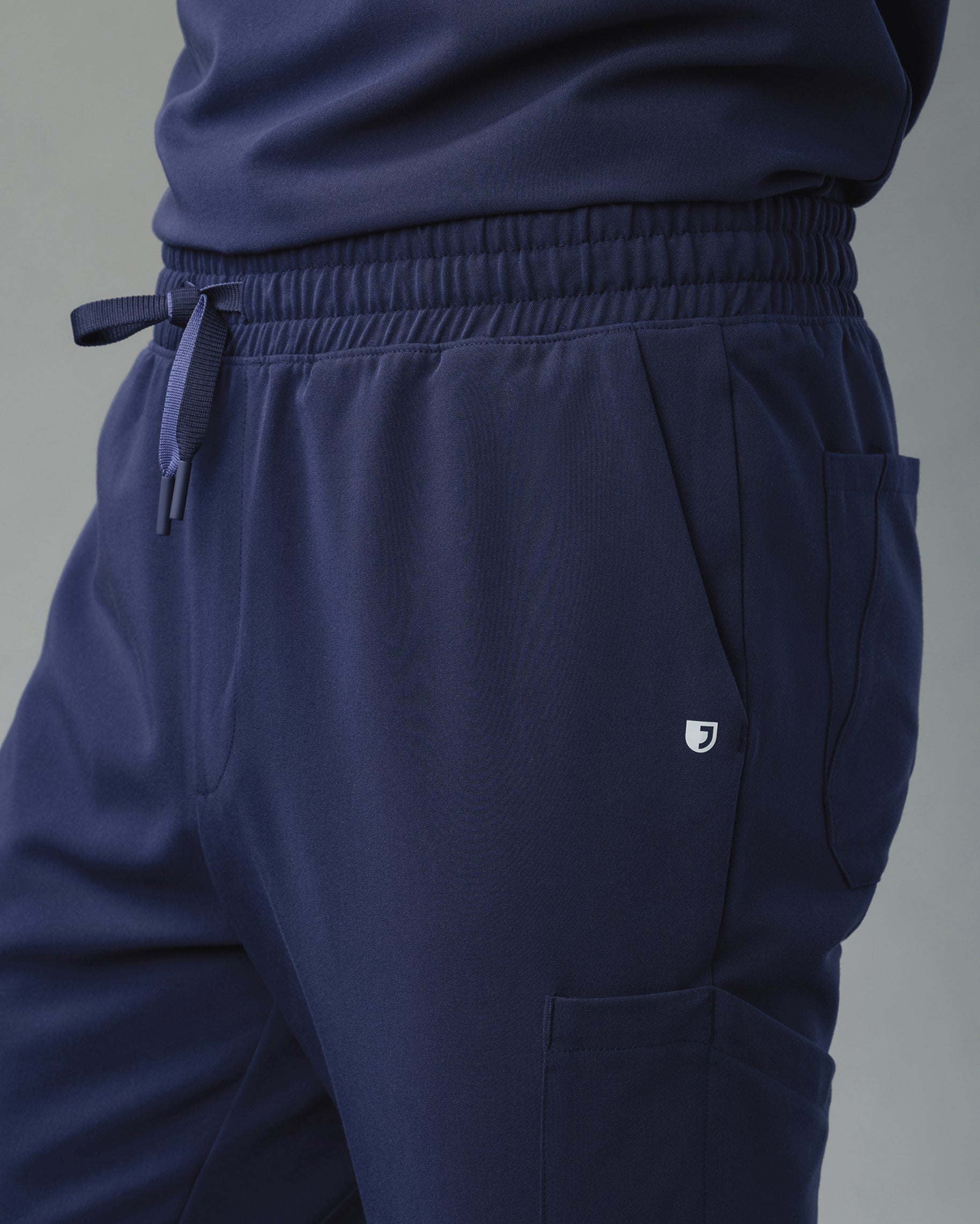 Close-up of the elastic waistband and drawstring of navy scrub joggers with a J logo by the pocket
