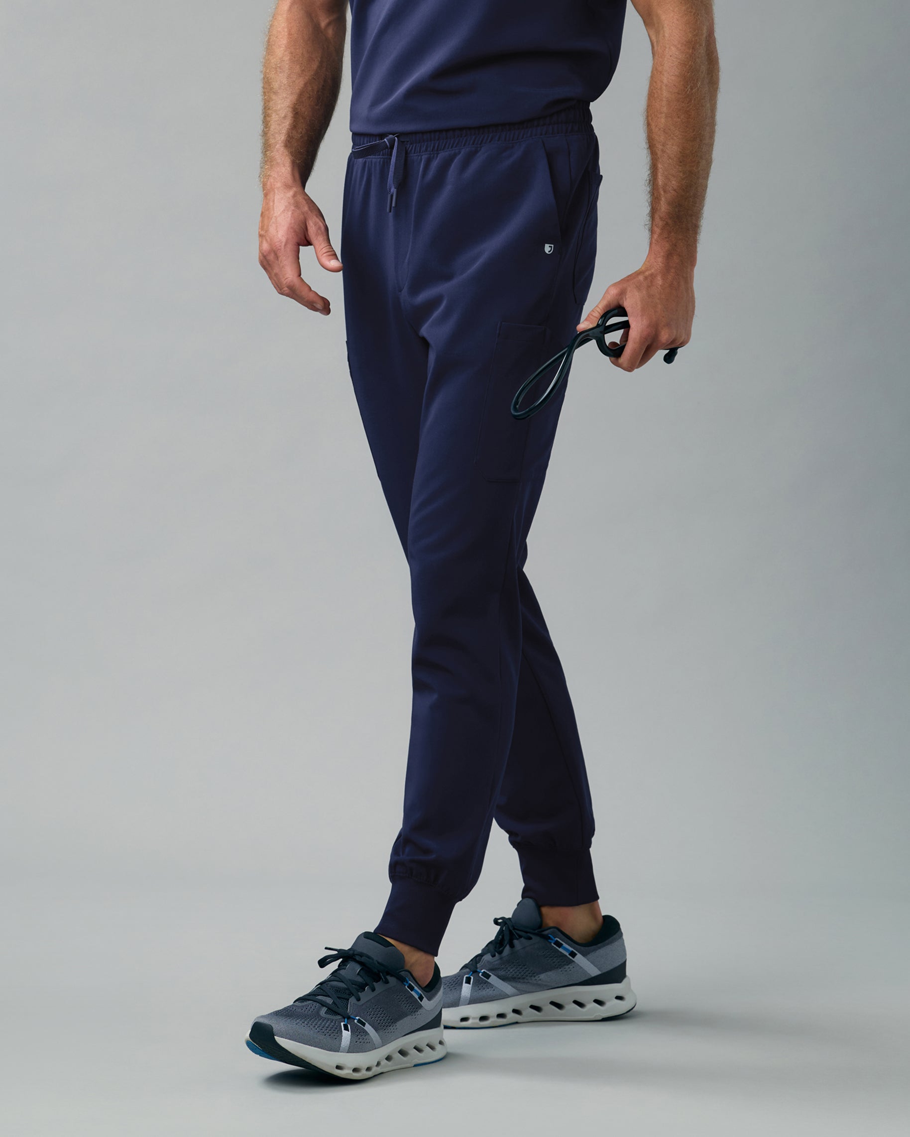 Man in navy slim scrub joggers with rib-knit cuffs, holding a stethoscope