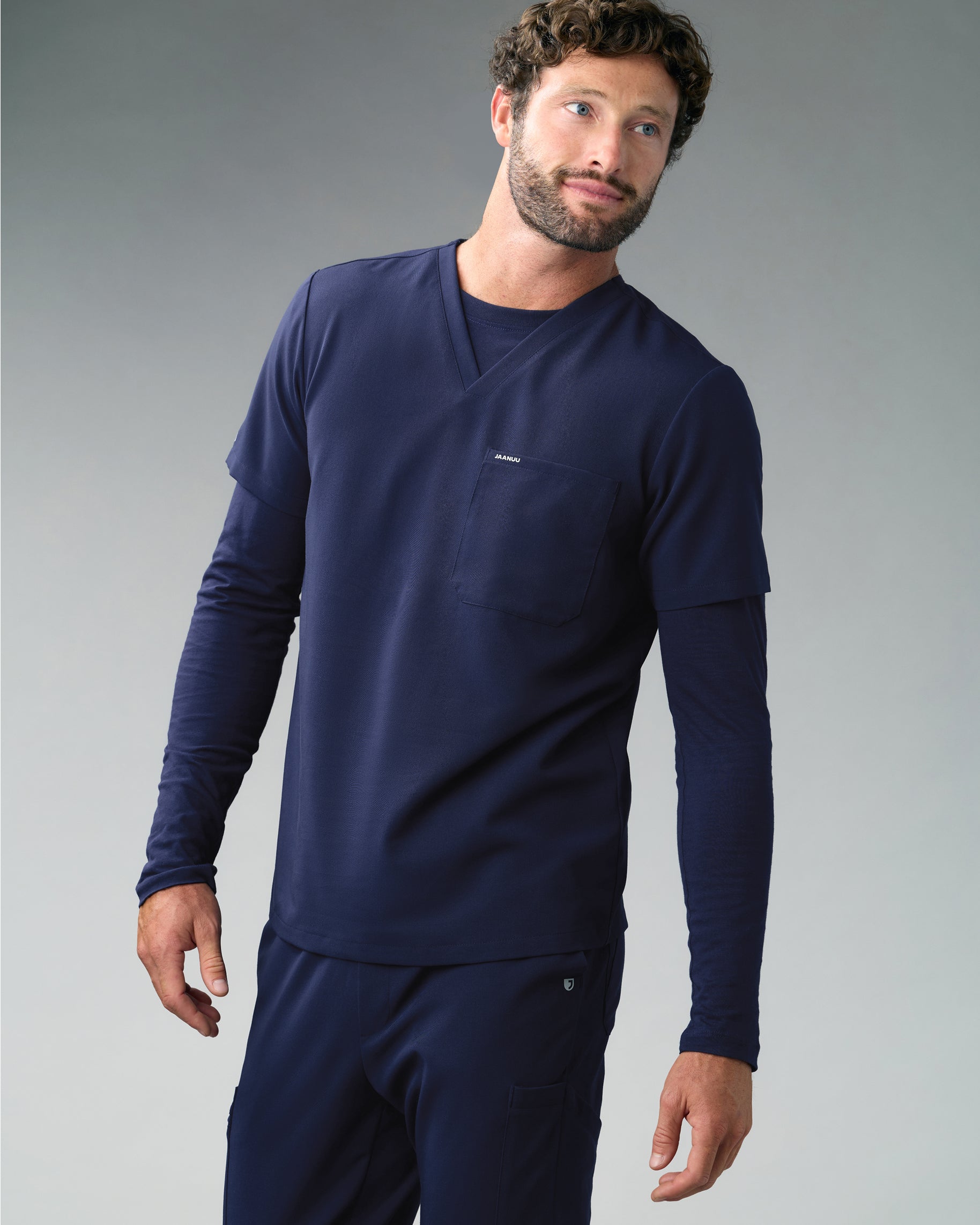 Man in a navy V-neck scrub top layered over a navy long-sleeve underscrub, with matching scrub pants