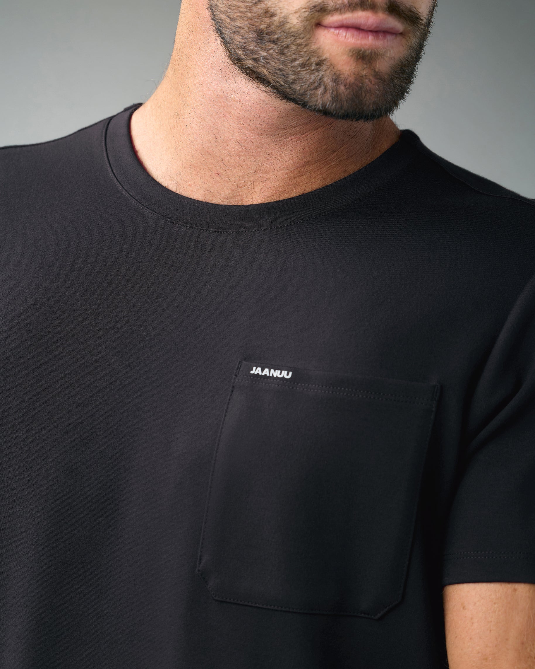 Close-up of the crew neck and chest pocket marked JAANUU on a black scrub top