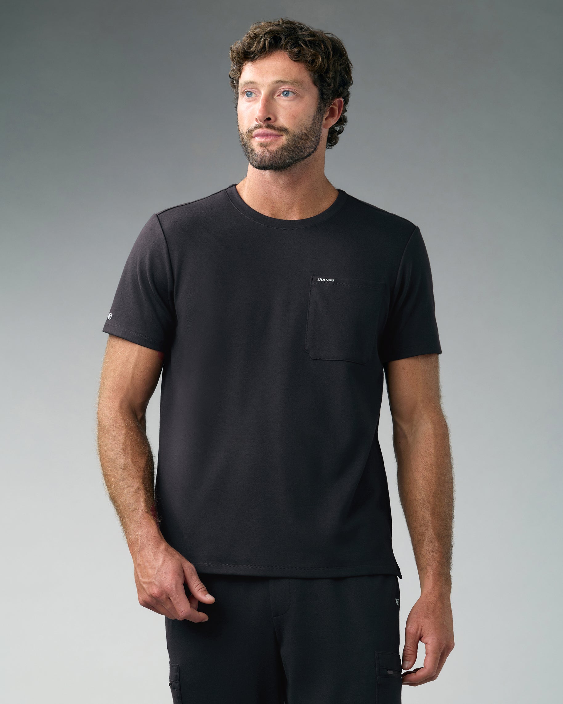 Man in a black crewneck scrub top with a chest pocket and matching cargo scrub pants