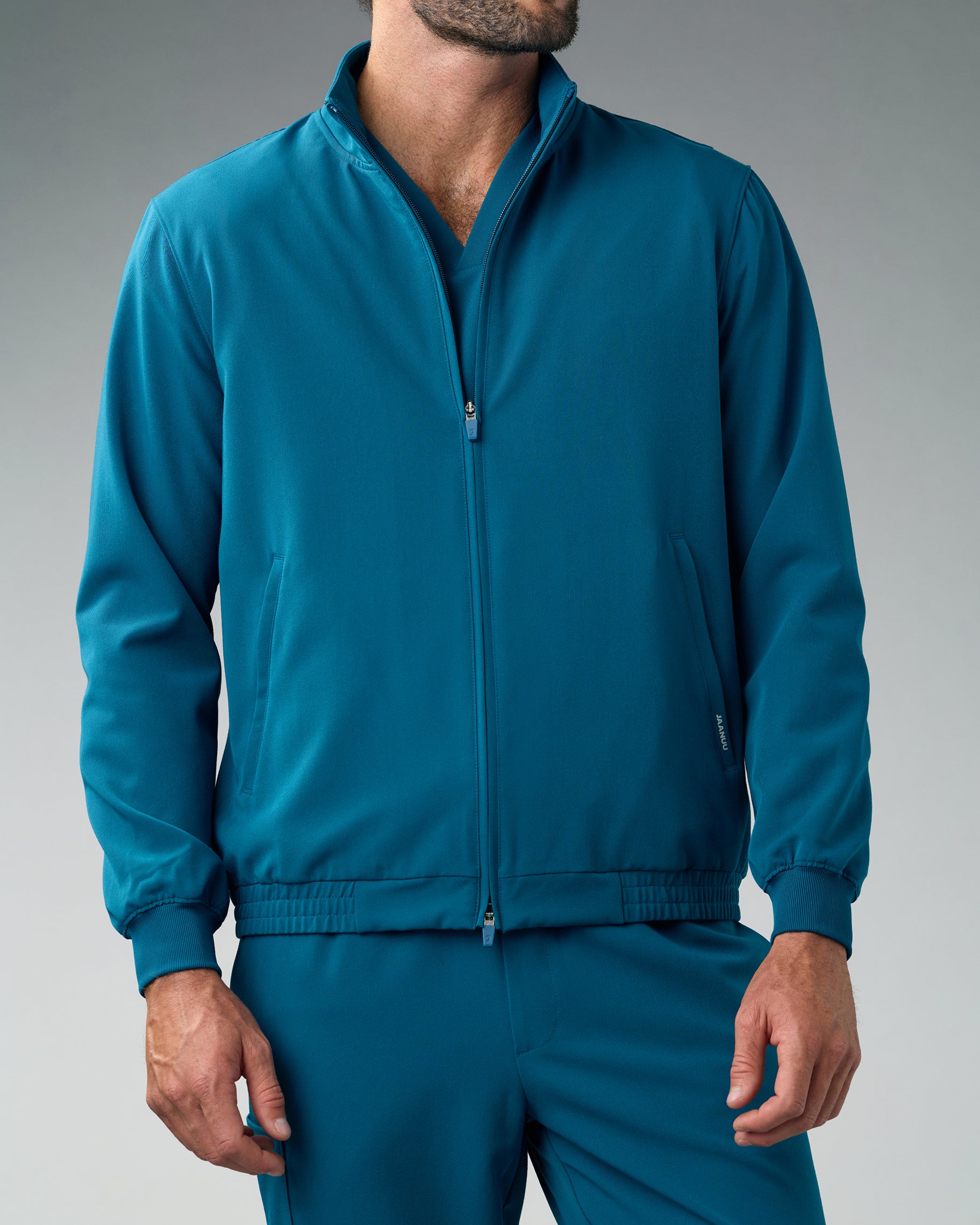 Man in a teal zip-up scrub jacket with an elastic hem and rib-knit cuffs over matching scrub pants