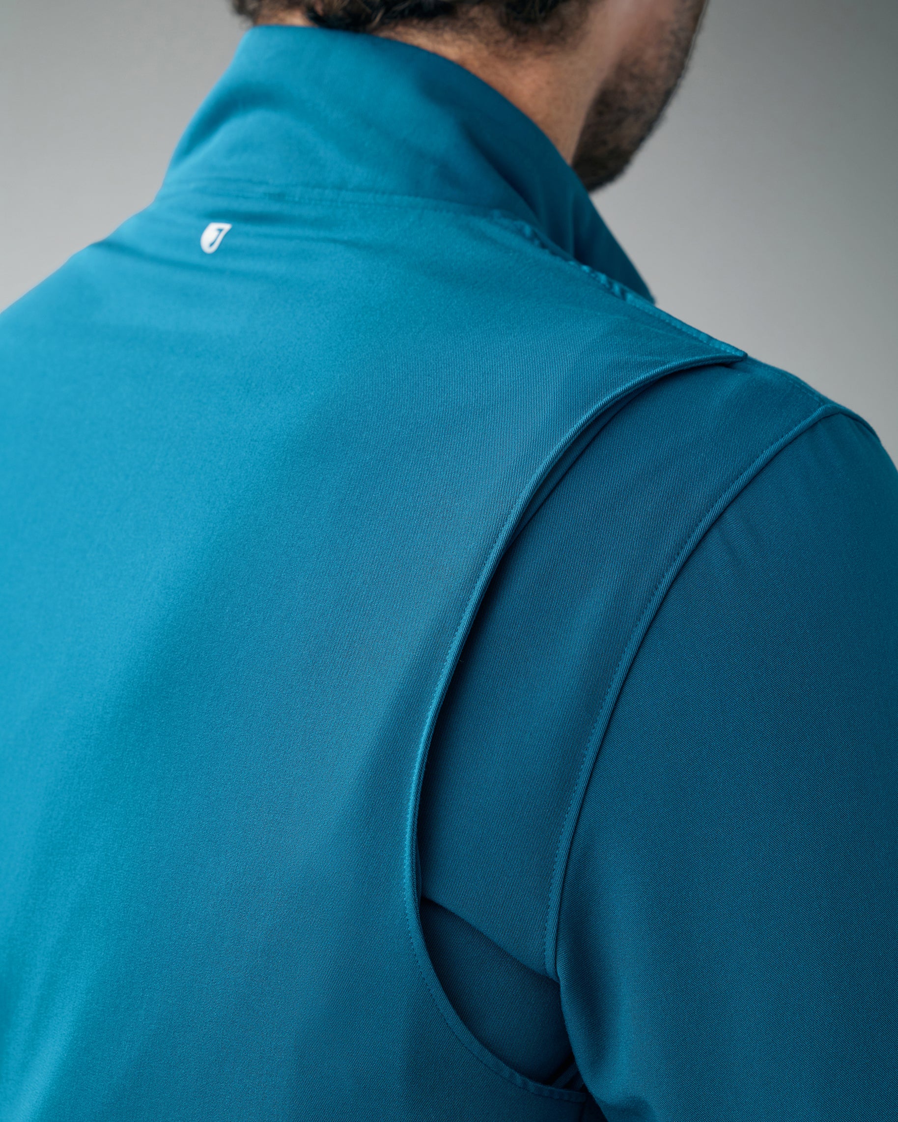Close-up of the bi-swing back panel of a teal scrub jacket with a J logo below the collar