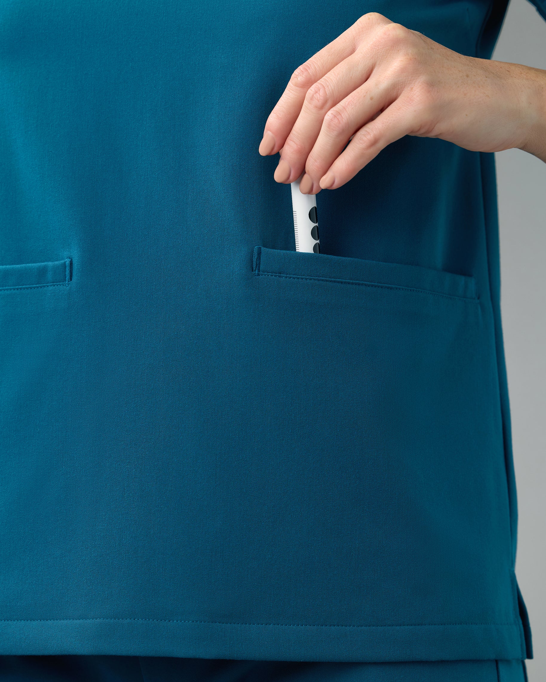 Close-up of a hand slipping a penlight into the front welt pocket of a teal scrub top