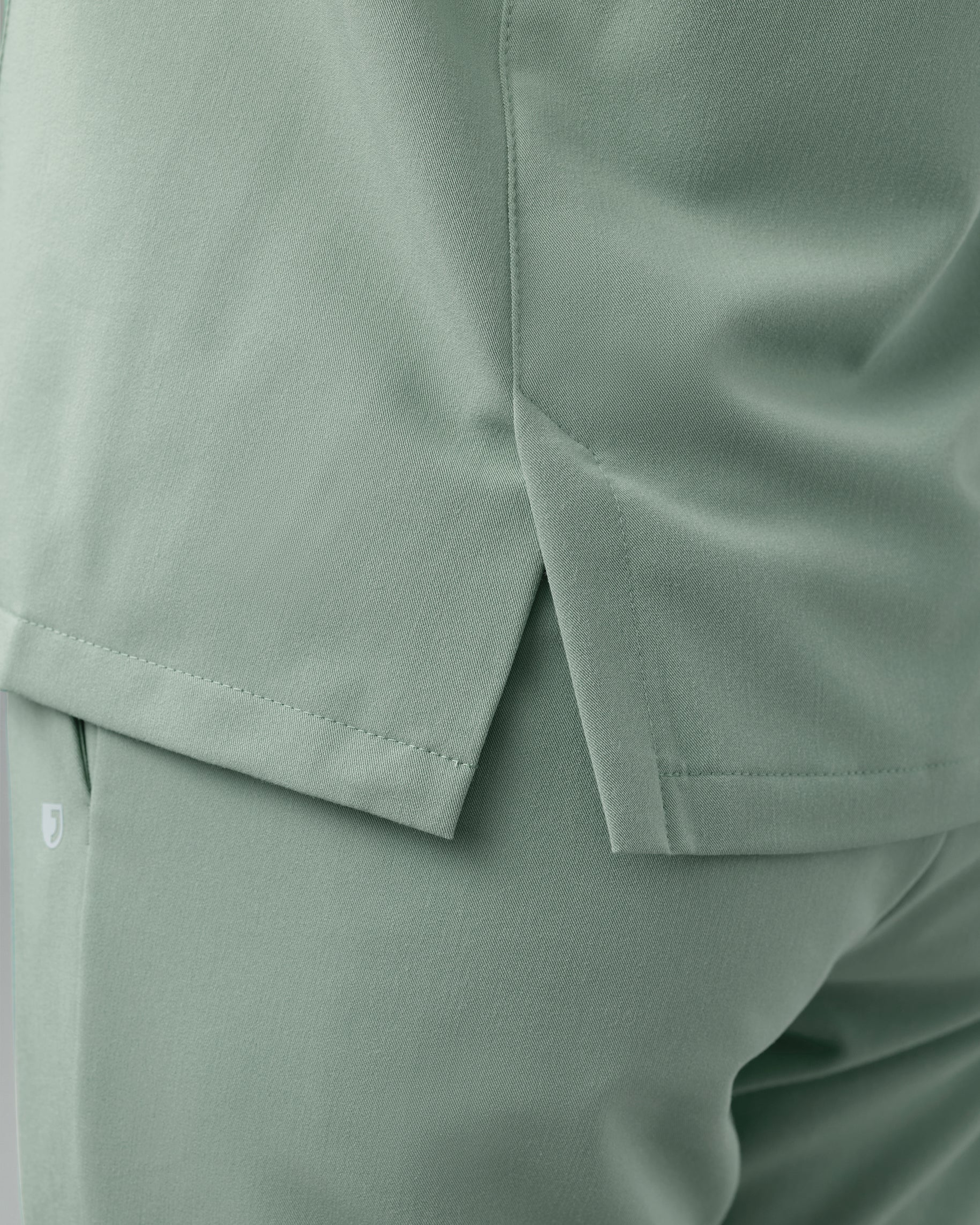 Close-up of the side vent at the hem of a sage green scrub top