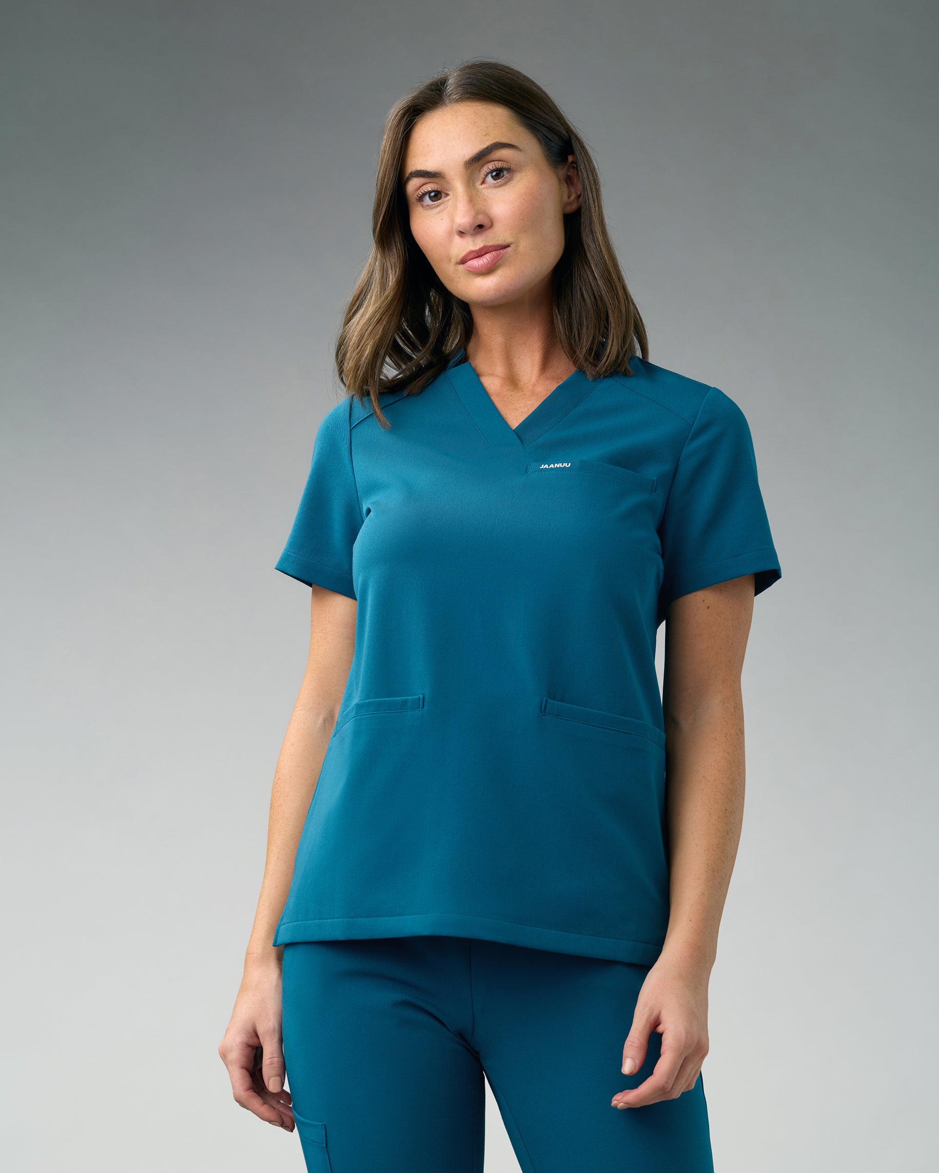 Woman in a teal slim notched V-neck scrub top with welt pockets and matching scrub pants
