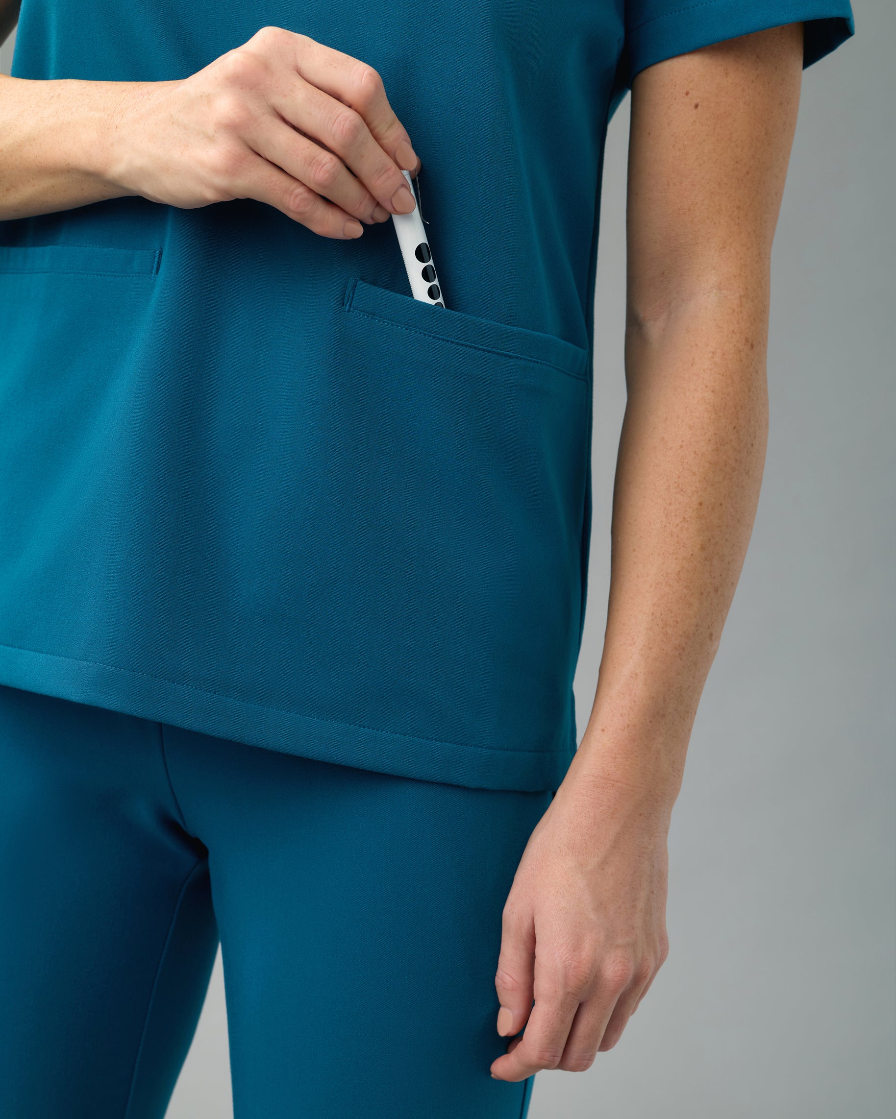 Close-up of a hand slipping a penlight into the front welt pocket of a teal slim scrub top