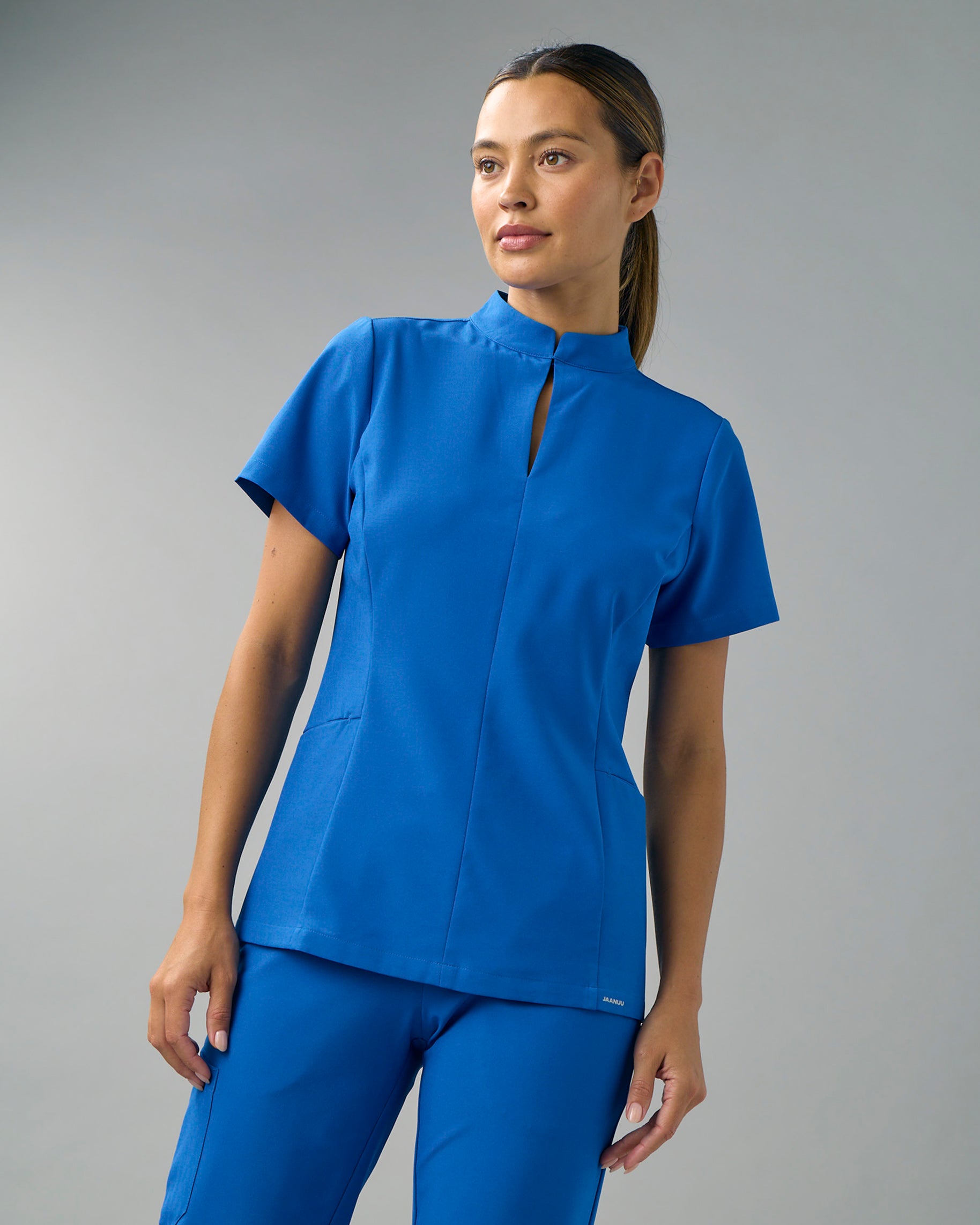 Woman in a royal blue mock-neck scrub top with a keyhole opening and a fitted waist, with matching scrub pants