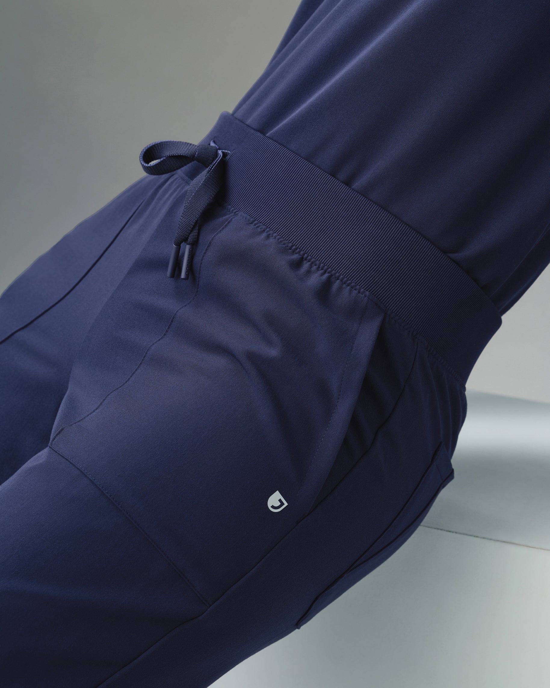 Close-up of the rib-knit waistband and drawstring of navy cargo scrub pants with a J logo by the pocket