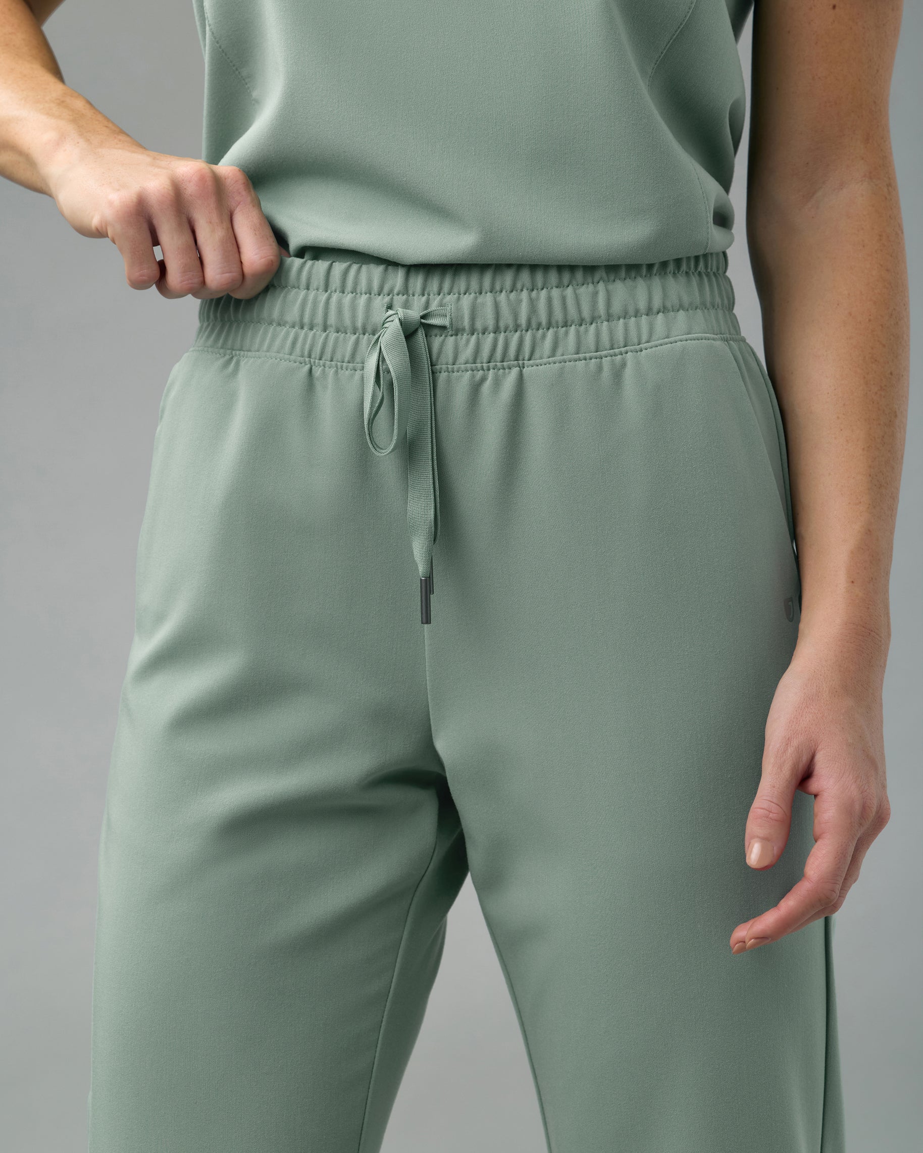 Close-up of the high elastic waistband and drawstring of sage green scrub pants