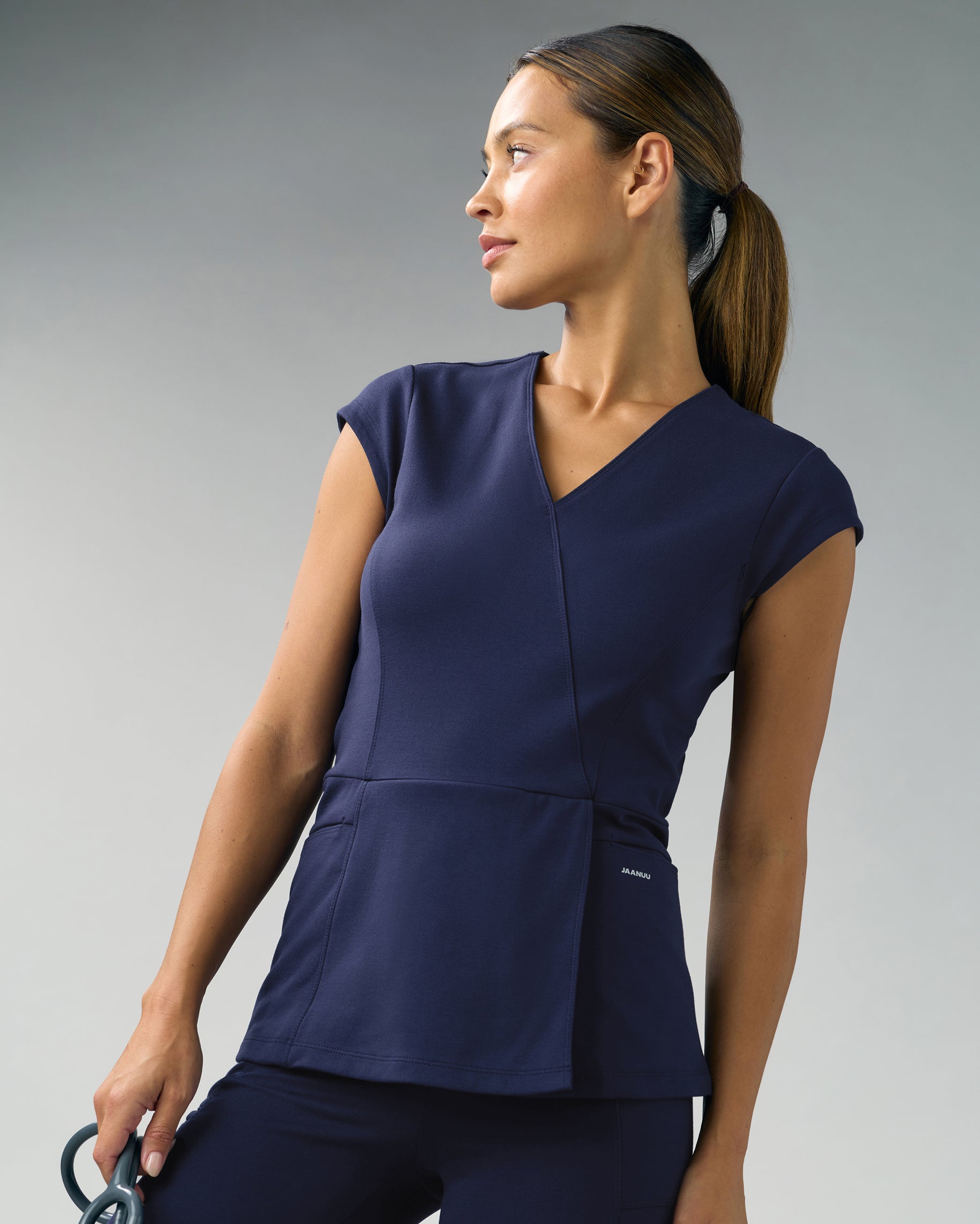 Woman in a navy mock-wrap scrub top with cap sleeves and matching scrub pants