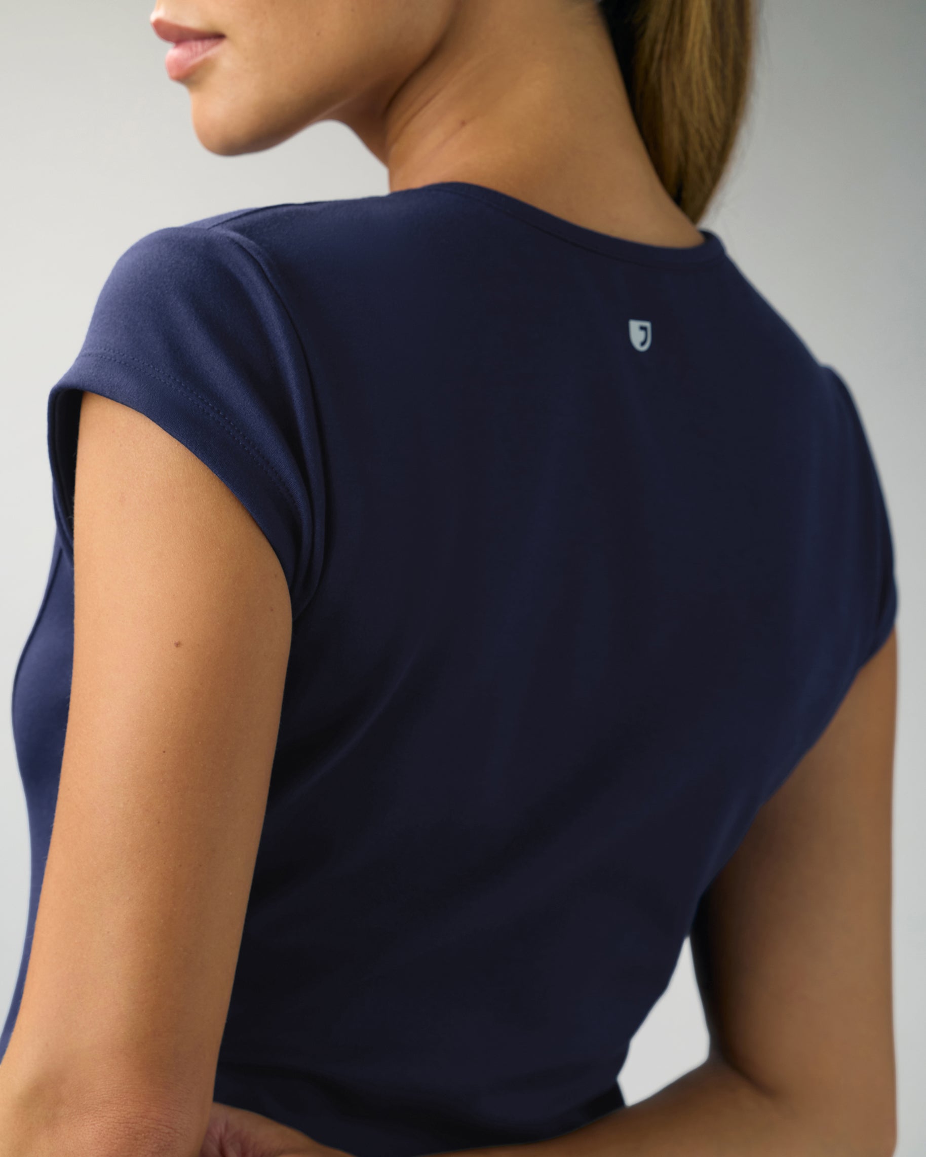 Back view of the cap sleeve of a navy scrub top with a J logo below the neckline