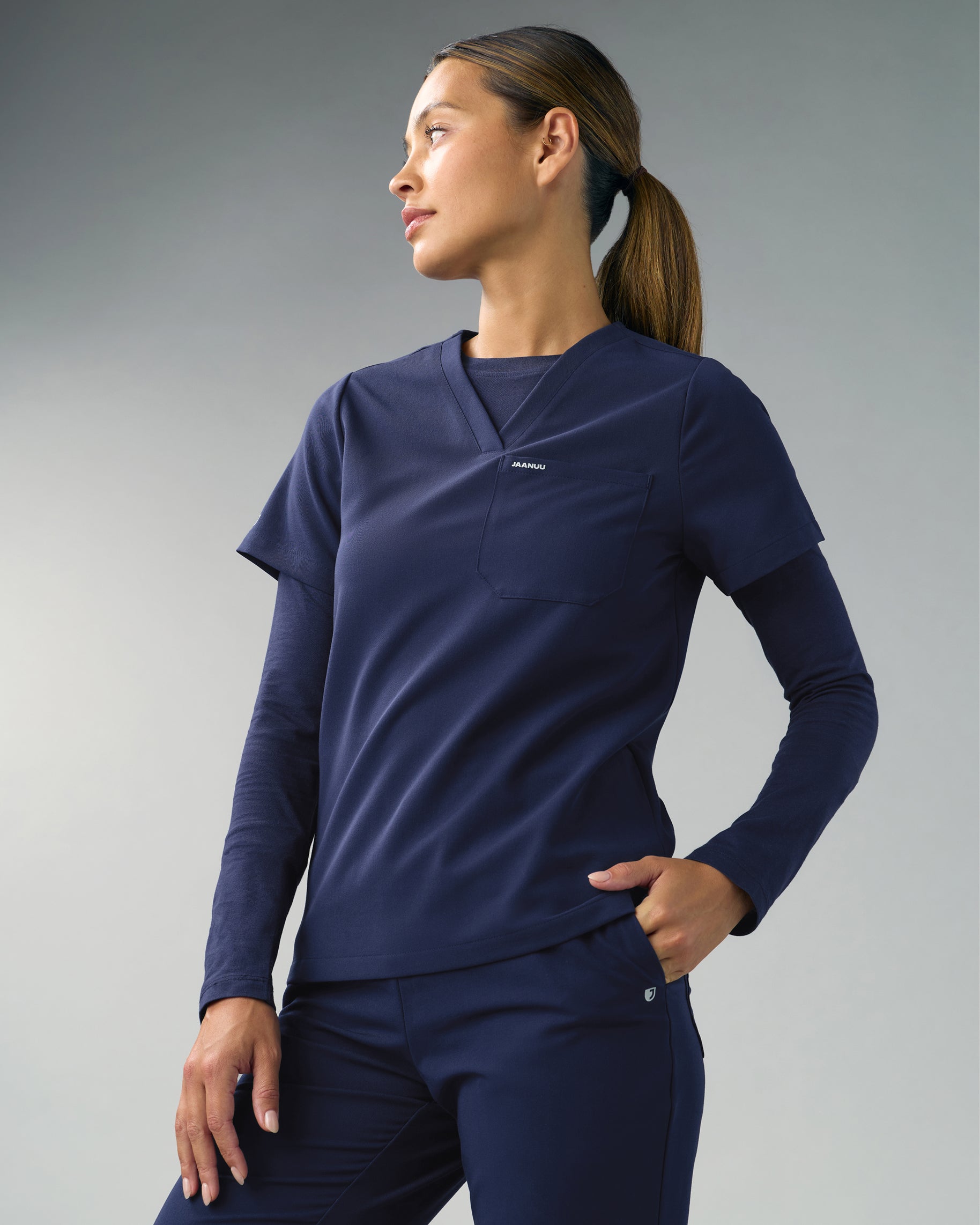Woman in a navy V-neck scrub top layered over a navy long-sleeve underscrub, with matching scrub pants
