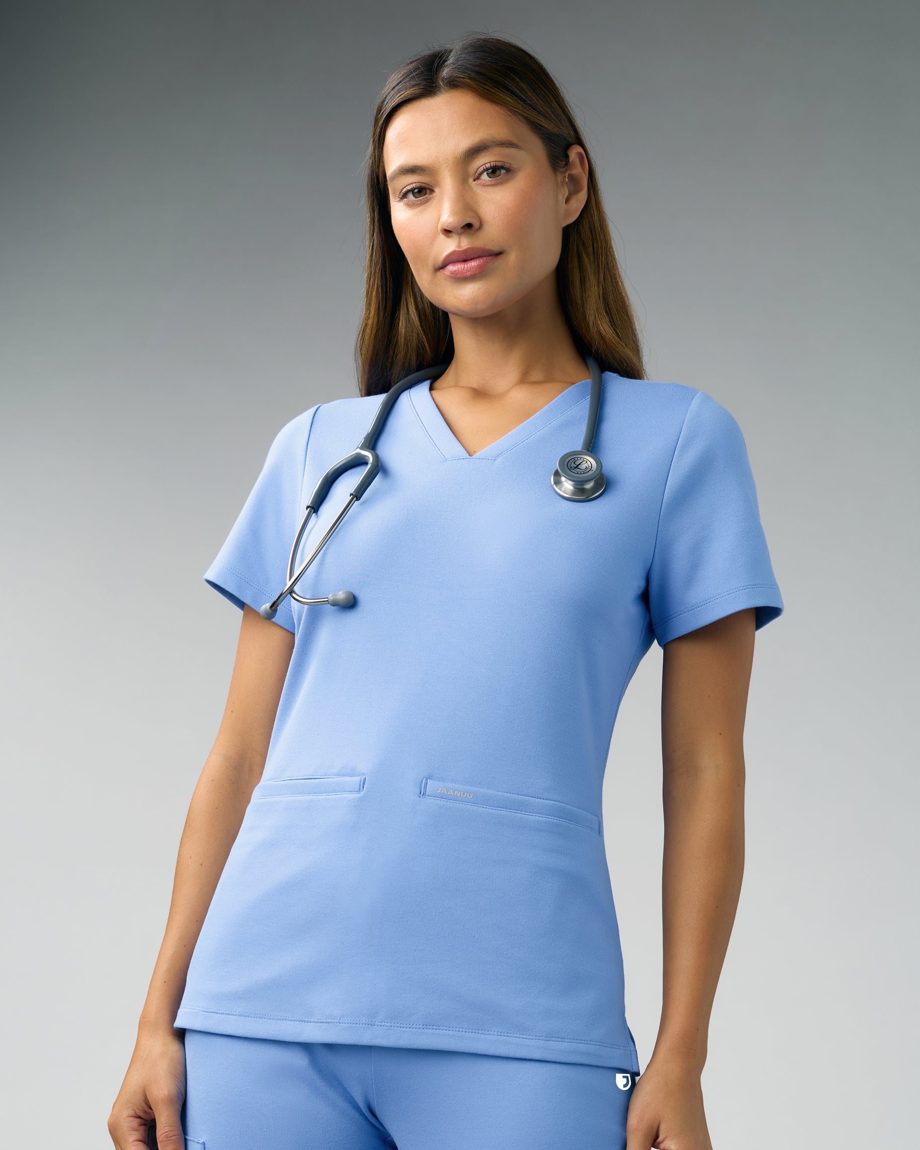 Woman in a light blue slim V-neck scrub top with two front welt pockets and a stethoscope around her neck
