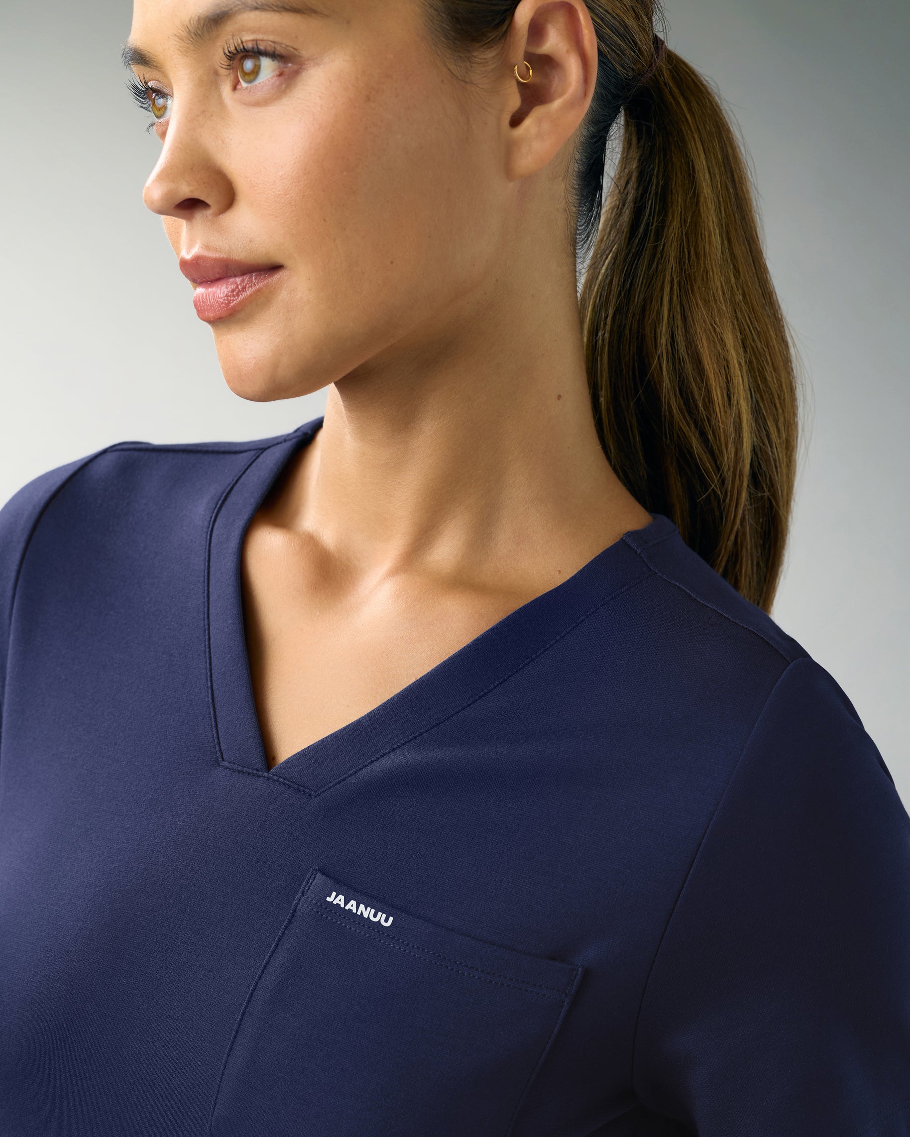 Woman in a navy V-neck scrub top with a chest pocket marked JAANUU