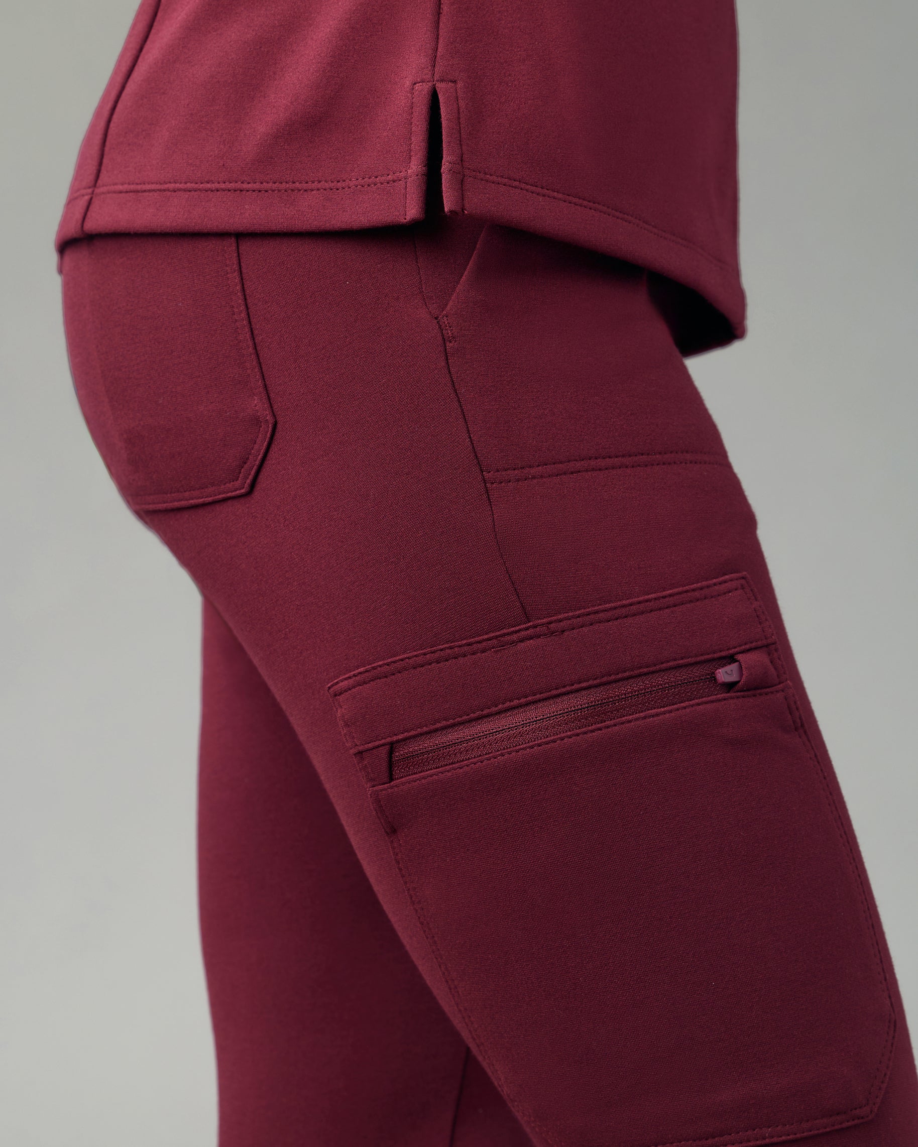 Close-up of the zippered cargo pocket and back patch pocket of burgundy skinny scrub joggers