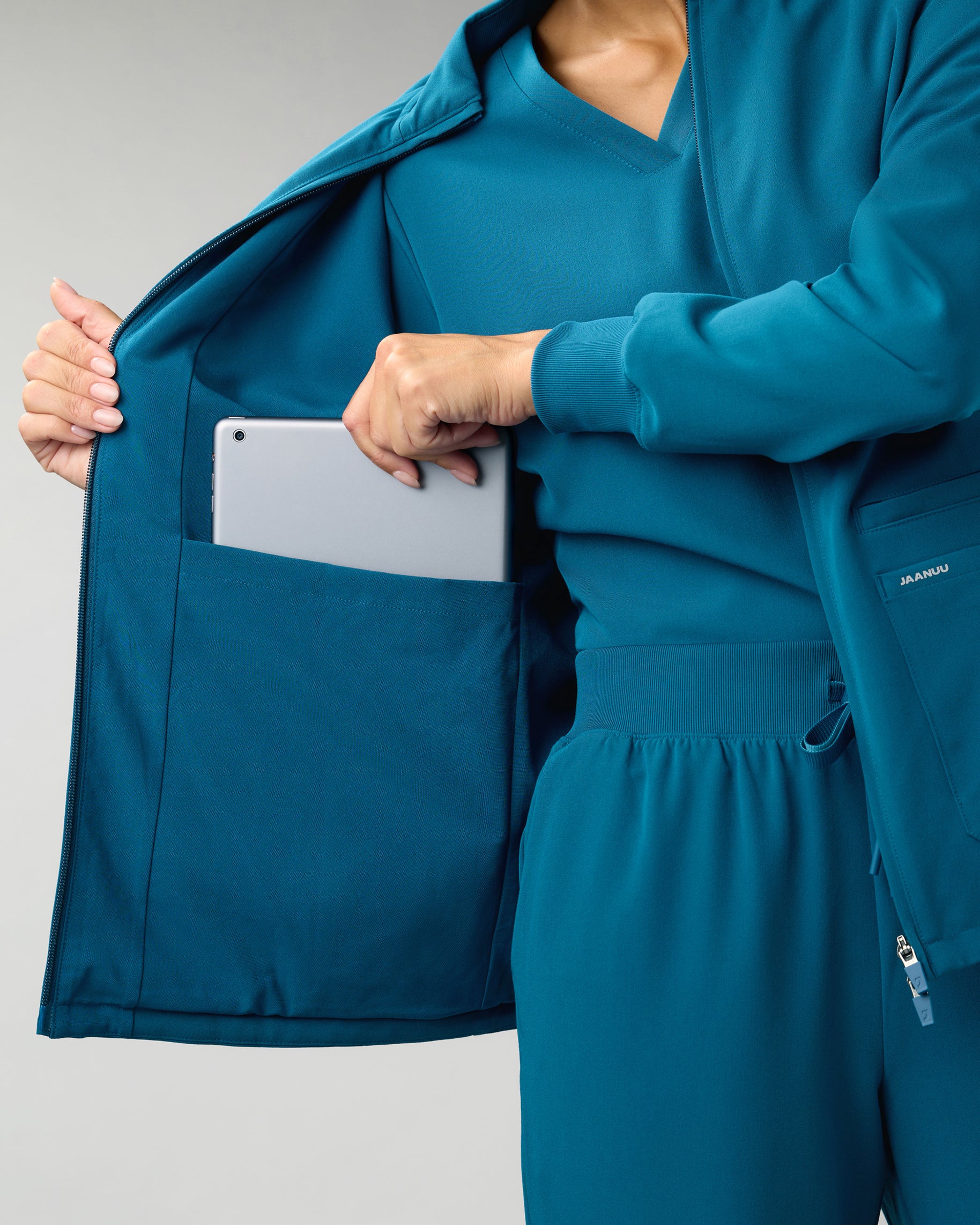 Woman sliding a tablet into the interior pocket of an open teal scrub jacket
