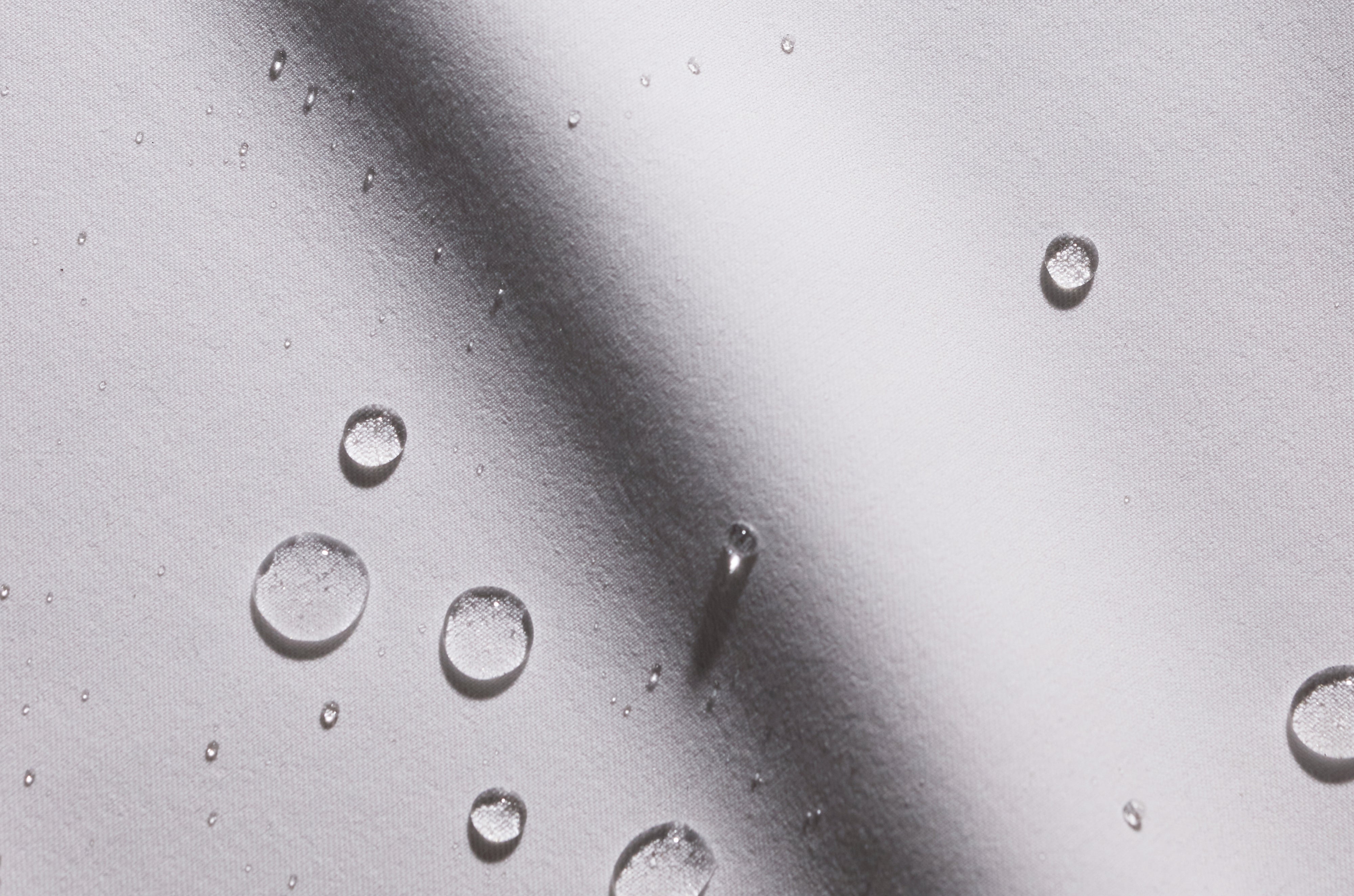 Close-up of water droplets beading on light gray Jaanuu UltraLAST+ fabric, with a soft diagonal shadow across it