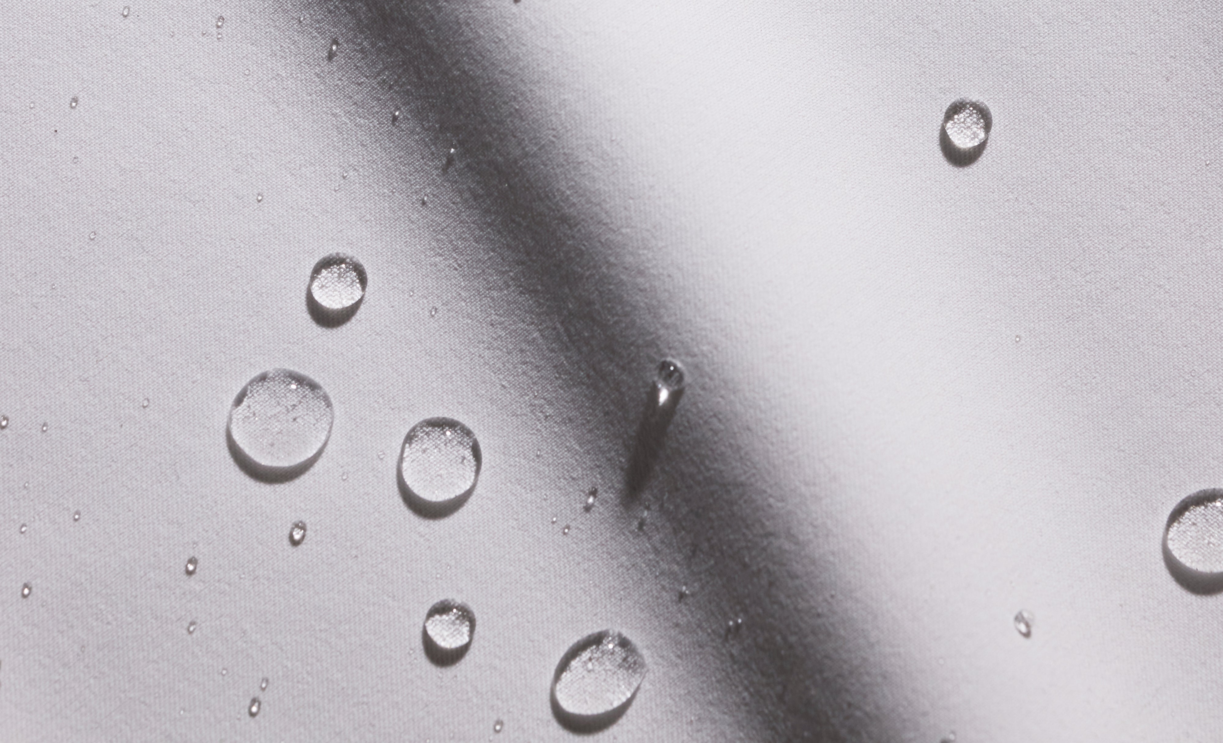 Close-up of water droplets beading on light gray Jaanuu UltraLAST+ fabric, with a soft diagonal shadow across it