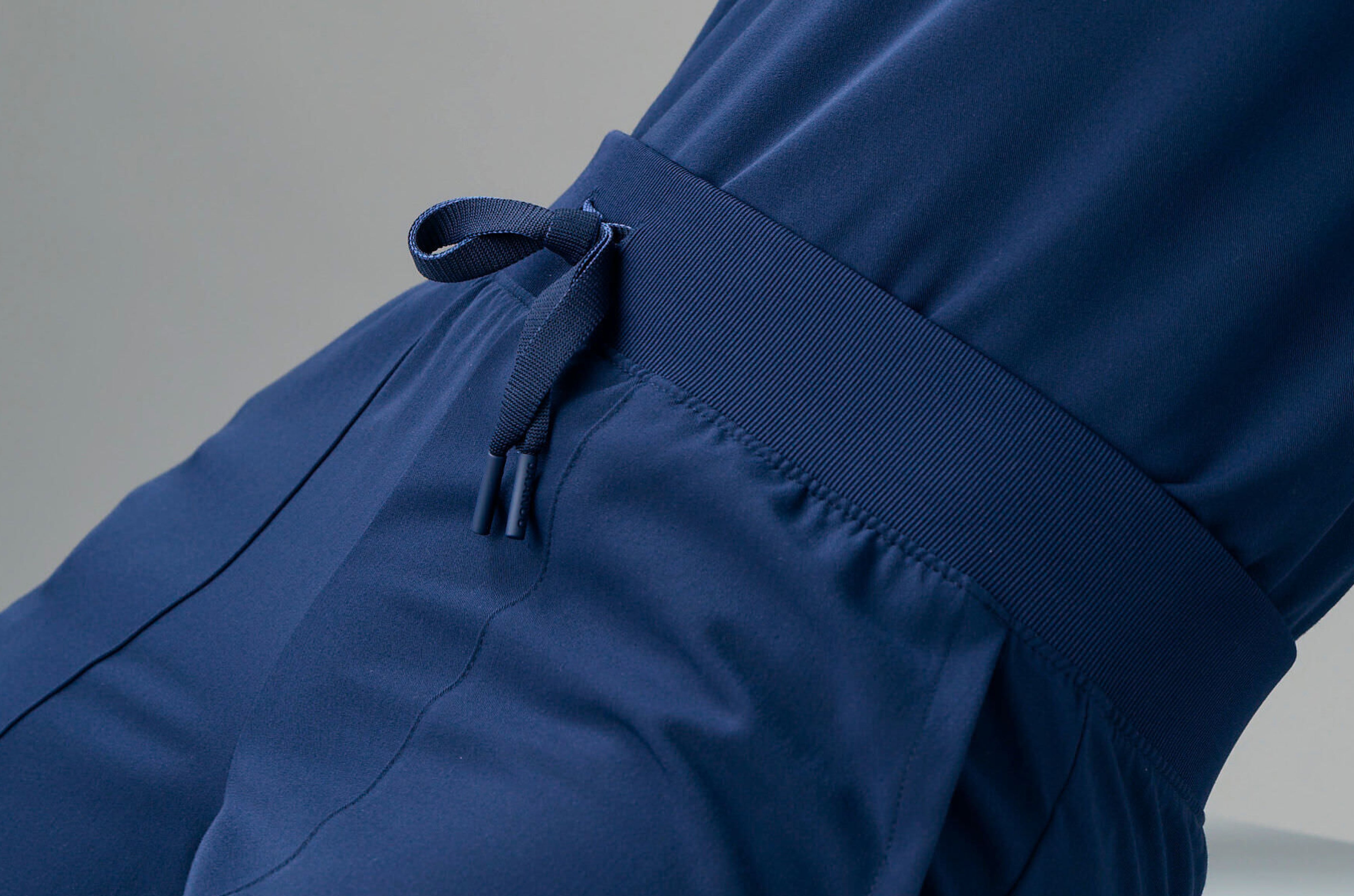 Close-up of the knit waistband and drawstring of navy blue Jaanuu scrub pants worn with a matching scrub top