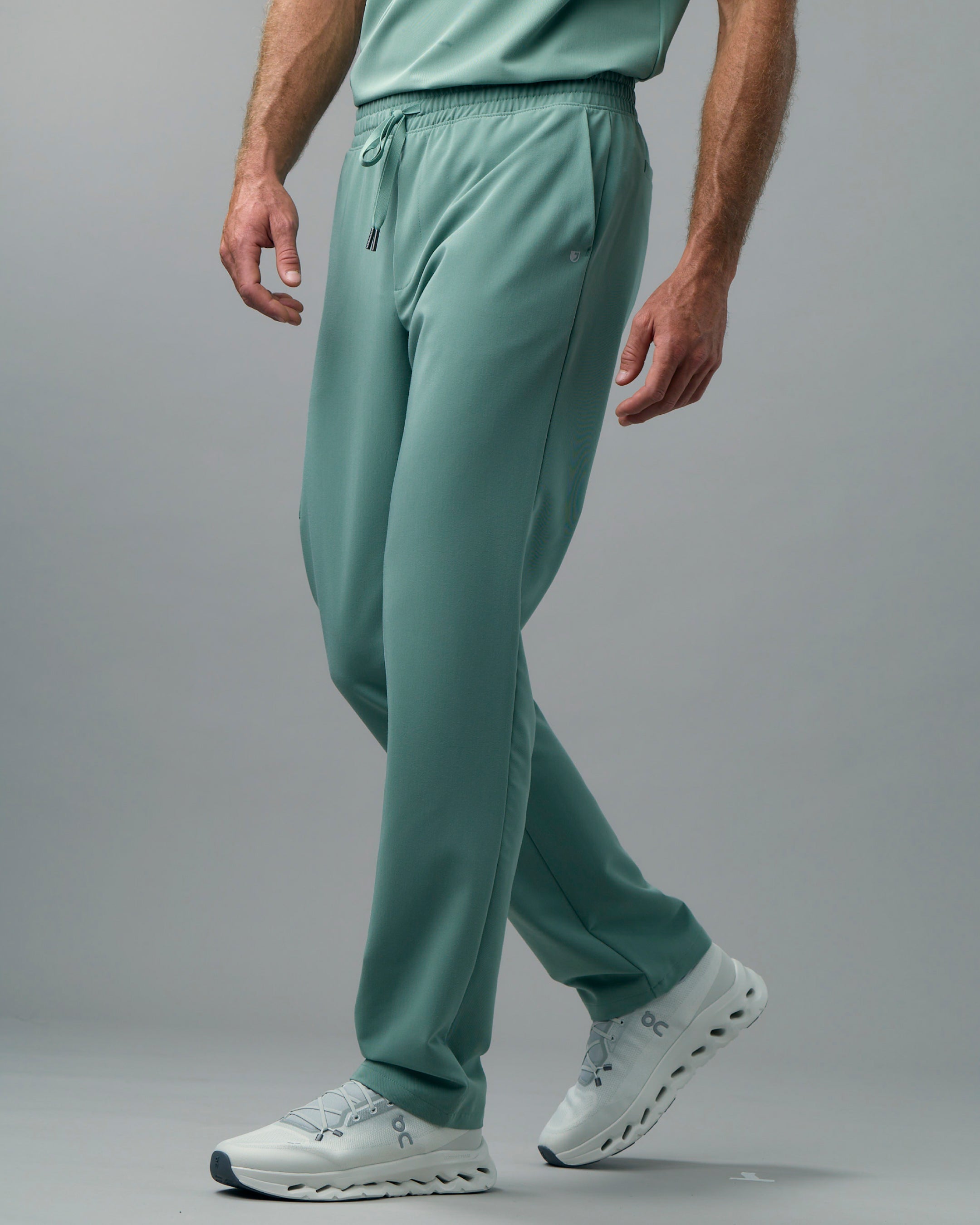 Man in green scrub pants and white sneakers mid-stride