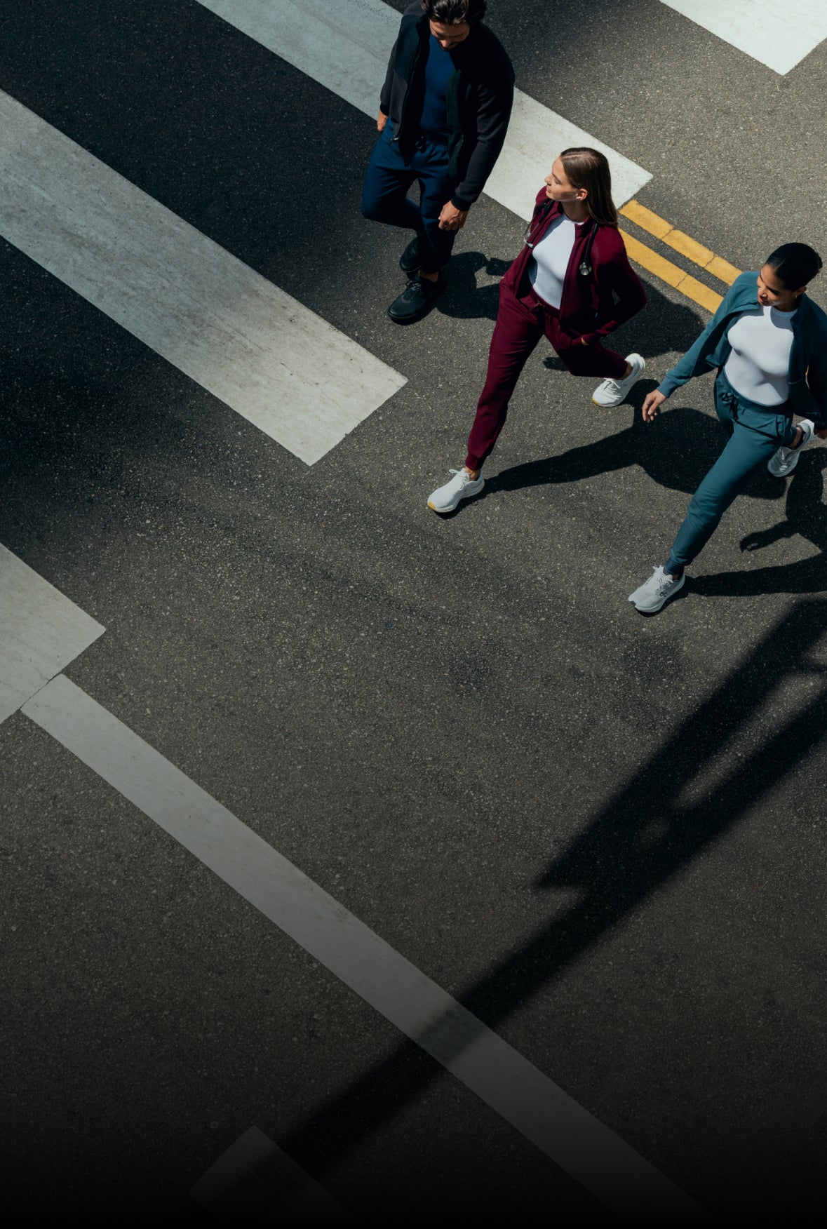 Three students in scrubs and jackets crossing a street, seen from above