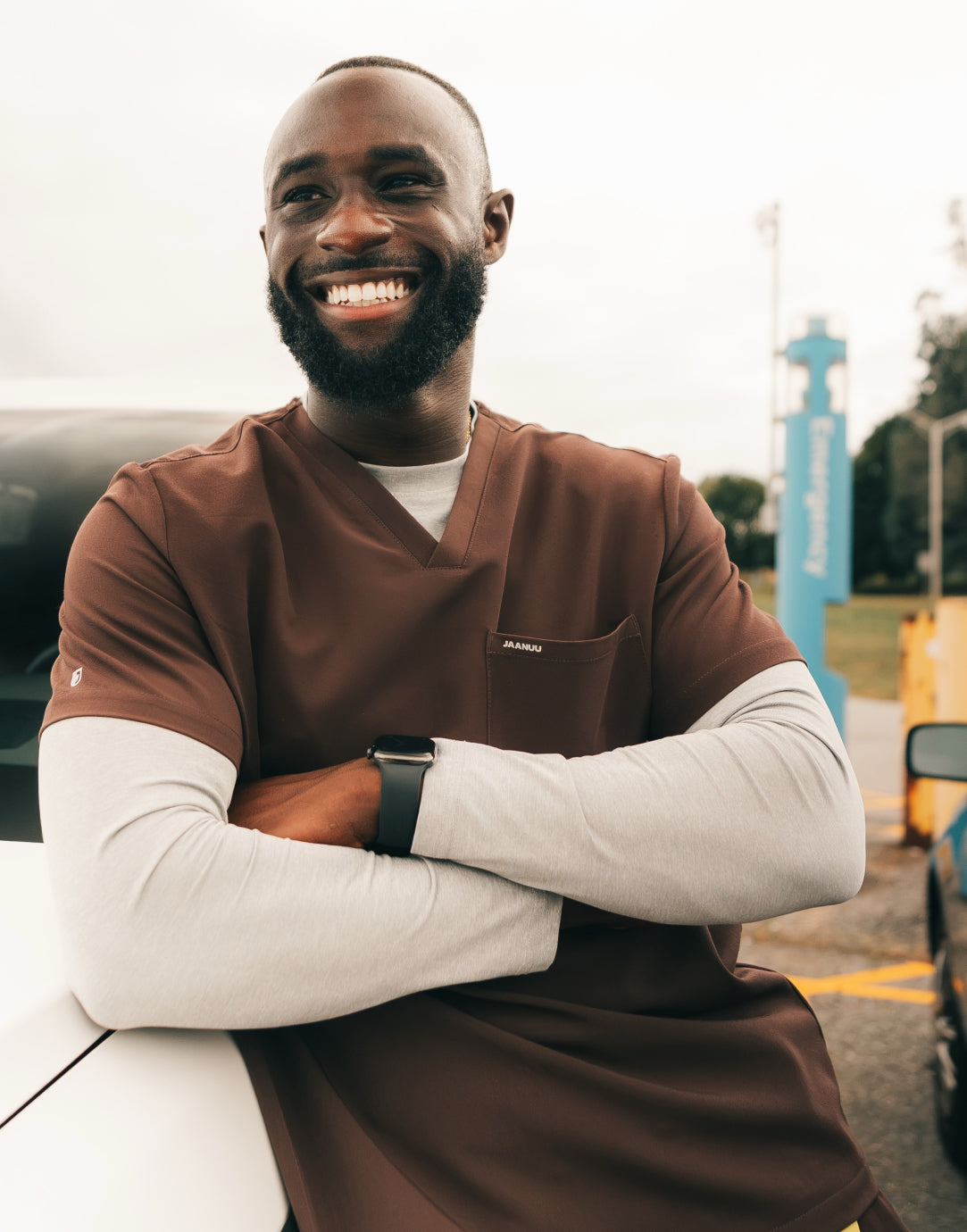 Smiling man in brown scrubs over a long-sleeve shirt with his arms crossed