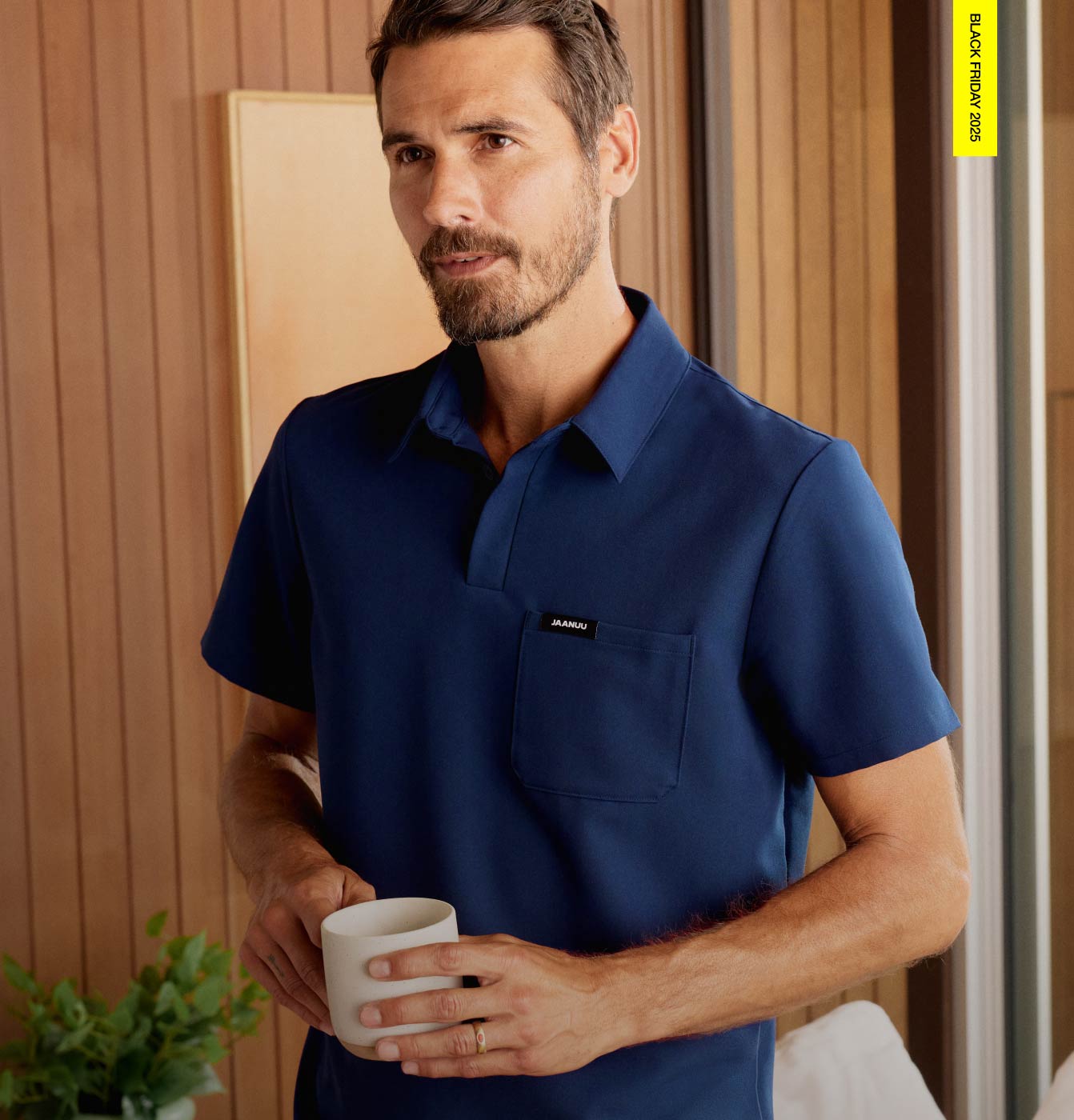 Image of man wearing a polo scrub top while holding a coffee mug. Image has text in the top right corner saying, "Black Friday 2025"