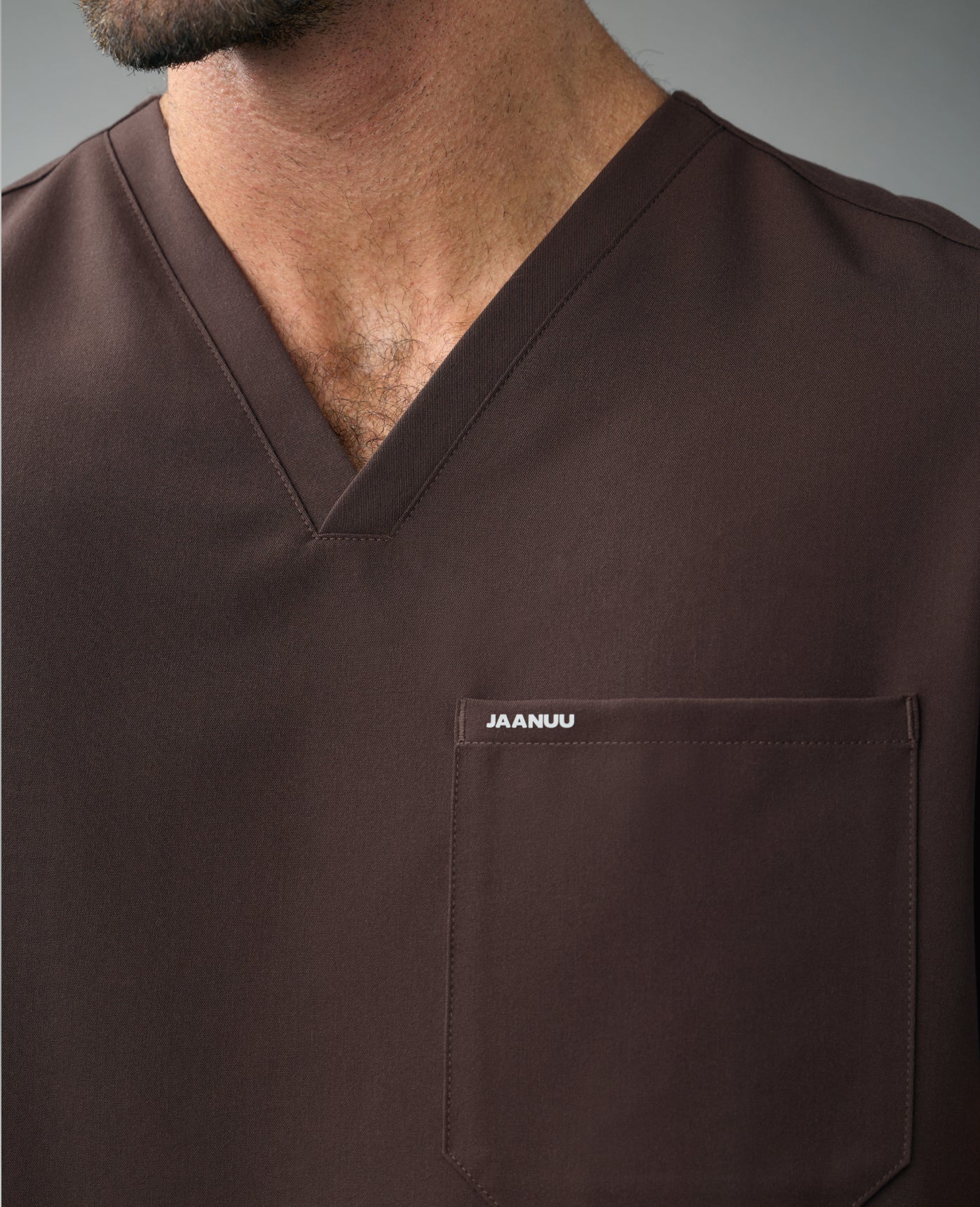 Close-up of a man in an Espresso Jaanuu V-neck scrub top with a chest pocket