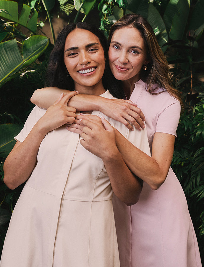 2 women wearing scrubs hugging each other.