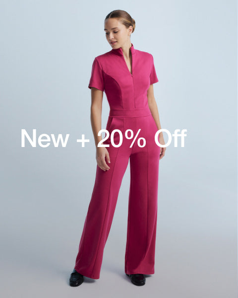 Image of a woman wearing a JAANUU scrub jumpsuit in the color, Wild Berry. Image has text that says, "New + 20% Off" - Women Nav Tile