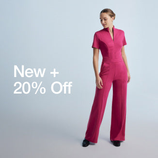 Image of a woman wearing a JAANUU scrub jumpsuit in the color, Wild Berry. Image has text that says, "New + 20% Off" - Women Nav Tile