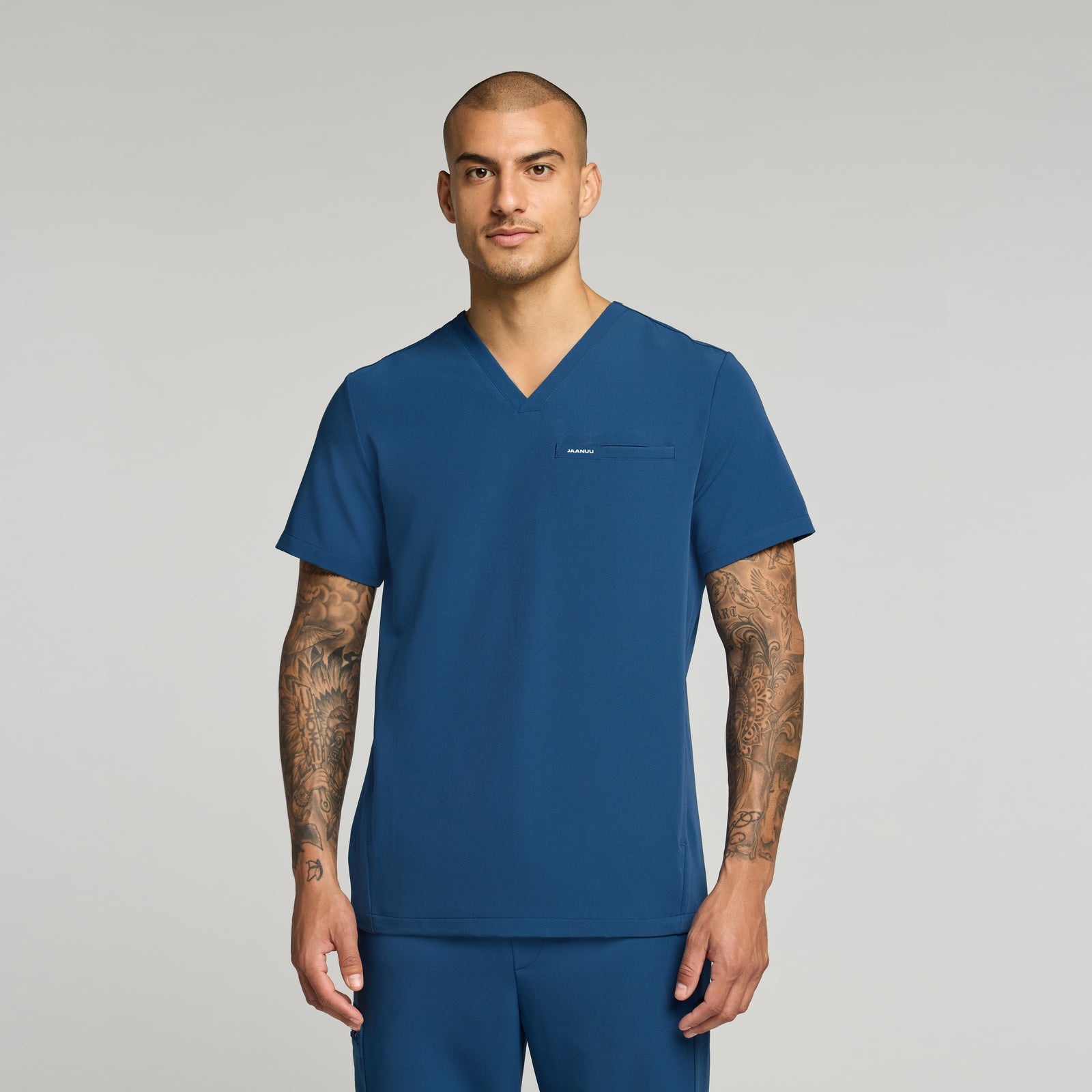 Man wearing a ocean colored scrub set against a gray background