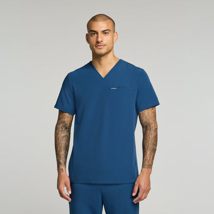 Man wearing a ocean colored scrub set against a gray background