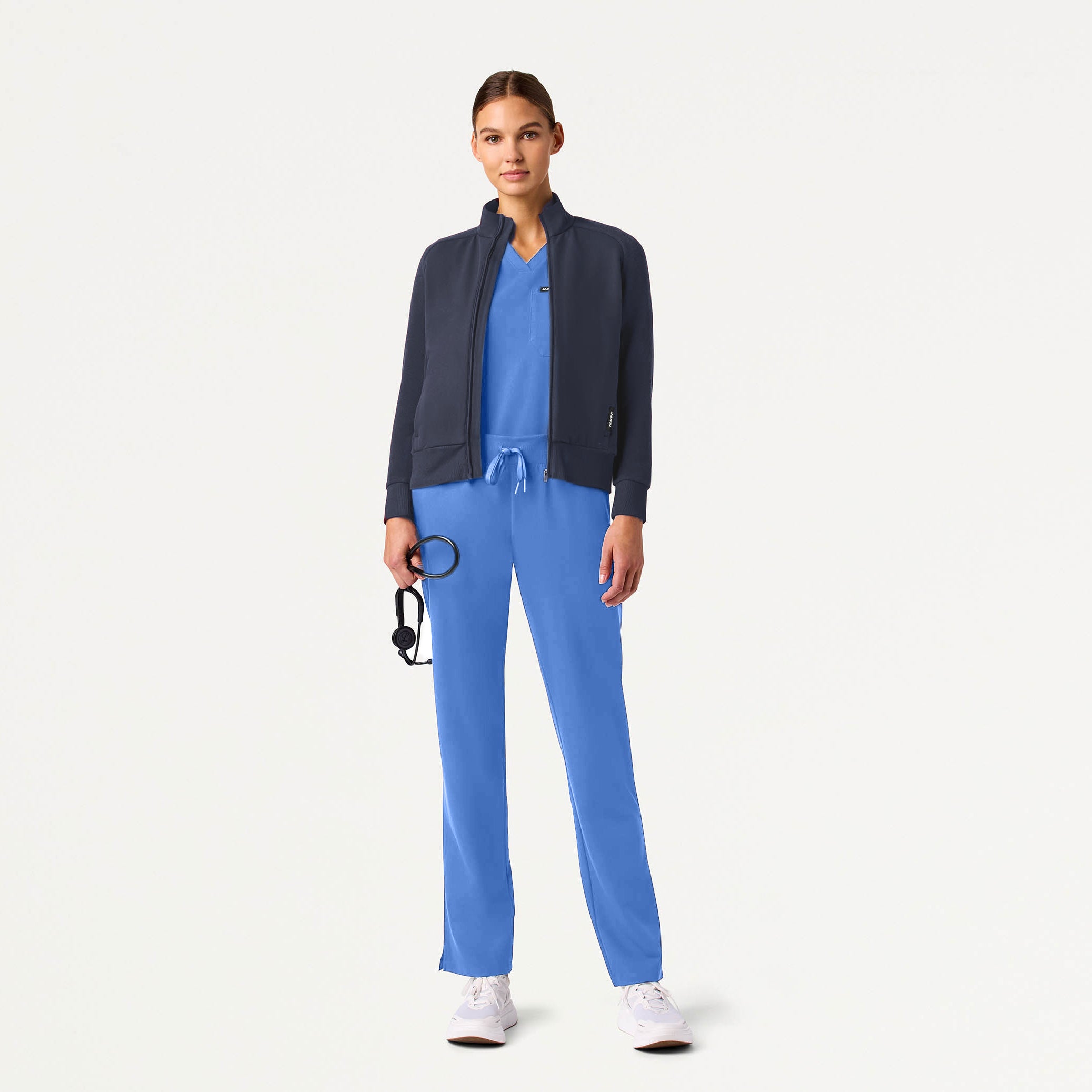 Person wearing a blue scrub set with a navy jacket on a white background