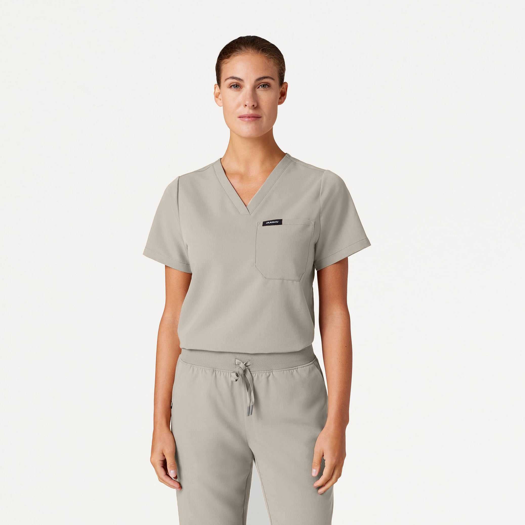 Person wearing a beige scrub set on a plain background
